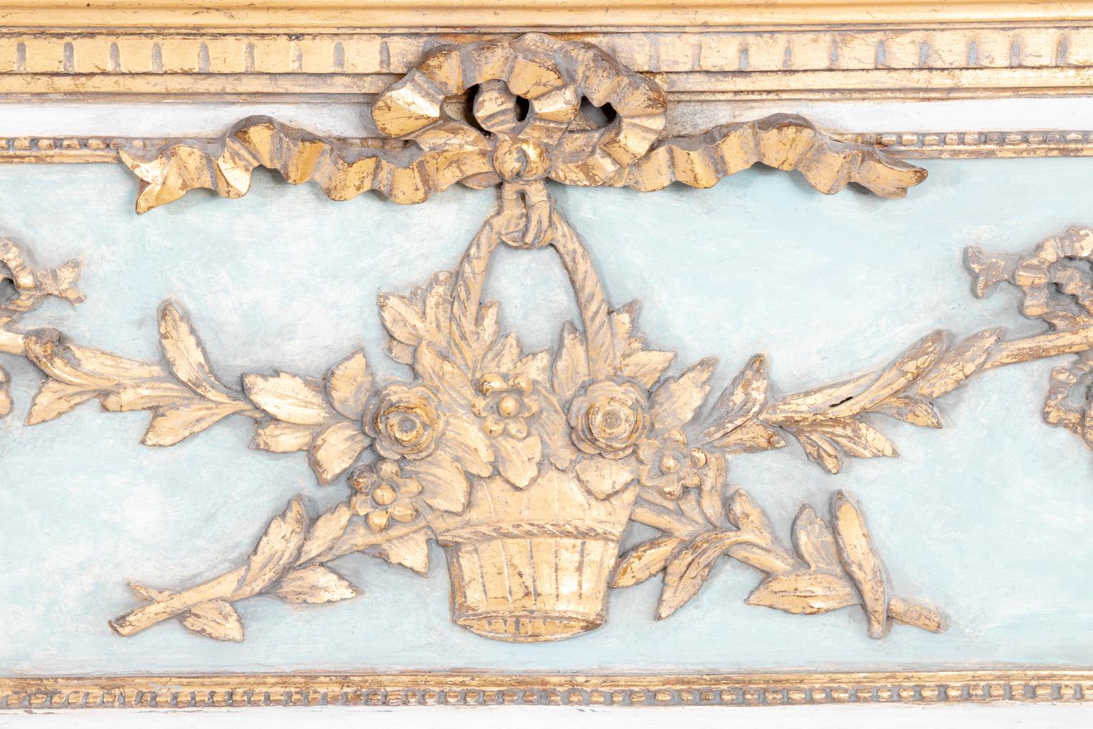 French trumeau mirror with a panel that features a carved basket of flowers with a bow ribbon, circa 1930s-1950s. The piece is also painted in blue, white, and gold. Please note of wear consistent with age including patina and wear to the edges.