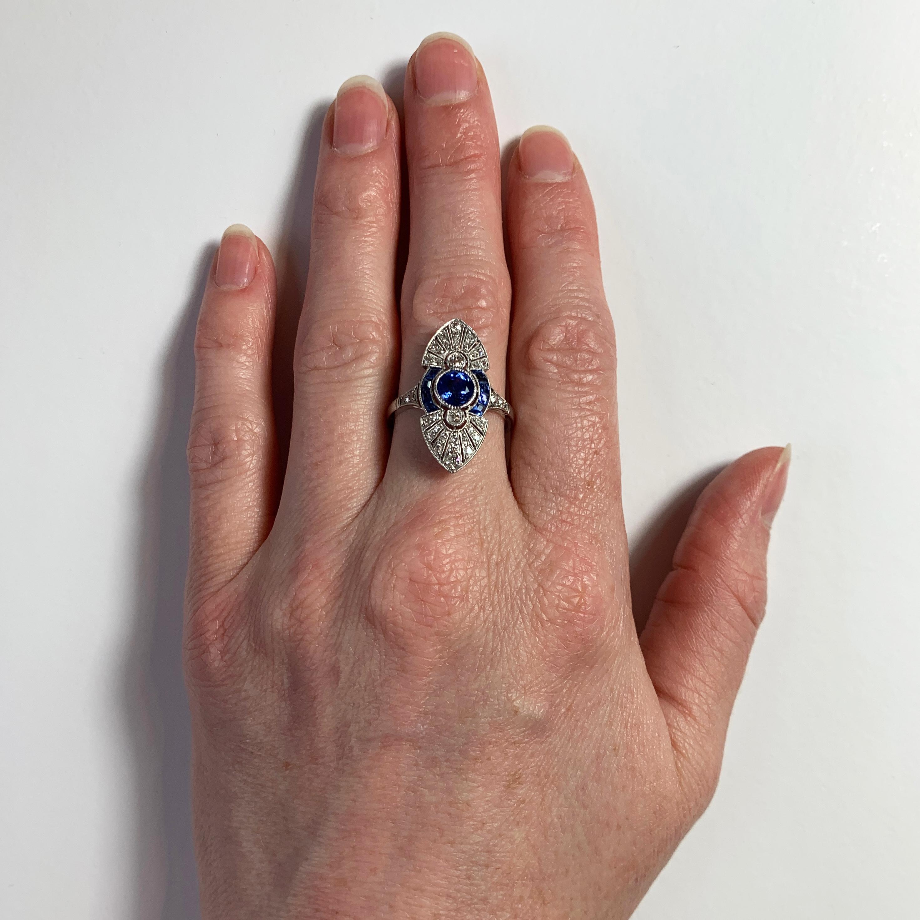 A French platinum, blue sapphire and diamond ring designed as an elongated marquise shape set with a central round mixed cut blue sapphire weighing approximately 0.95 carats, surrounded by eight calibré cut blue sapphires. The ring is further set