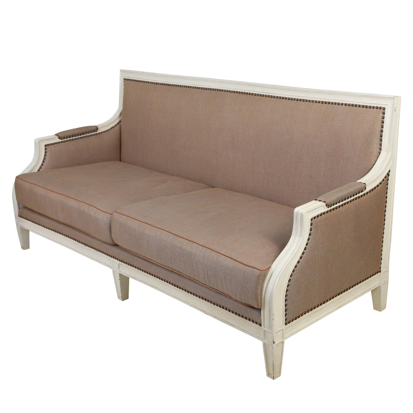 Ein altes französisches Sofa mit weißem Rahmen und dunkelbeigem Stoffbezug, fester Rückenlehne, zwei Sitzkissen, gepolsterten Armlehnen, Nagelkopfverzierungen und gerader Rückenlehne und Beinen.