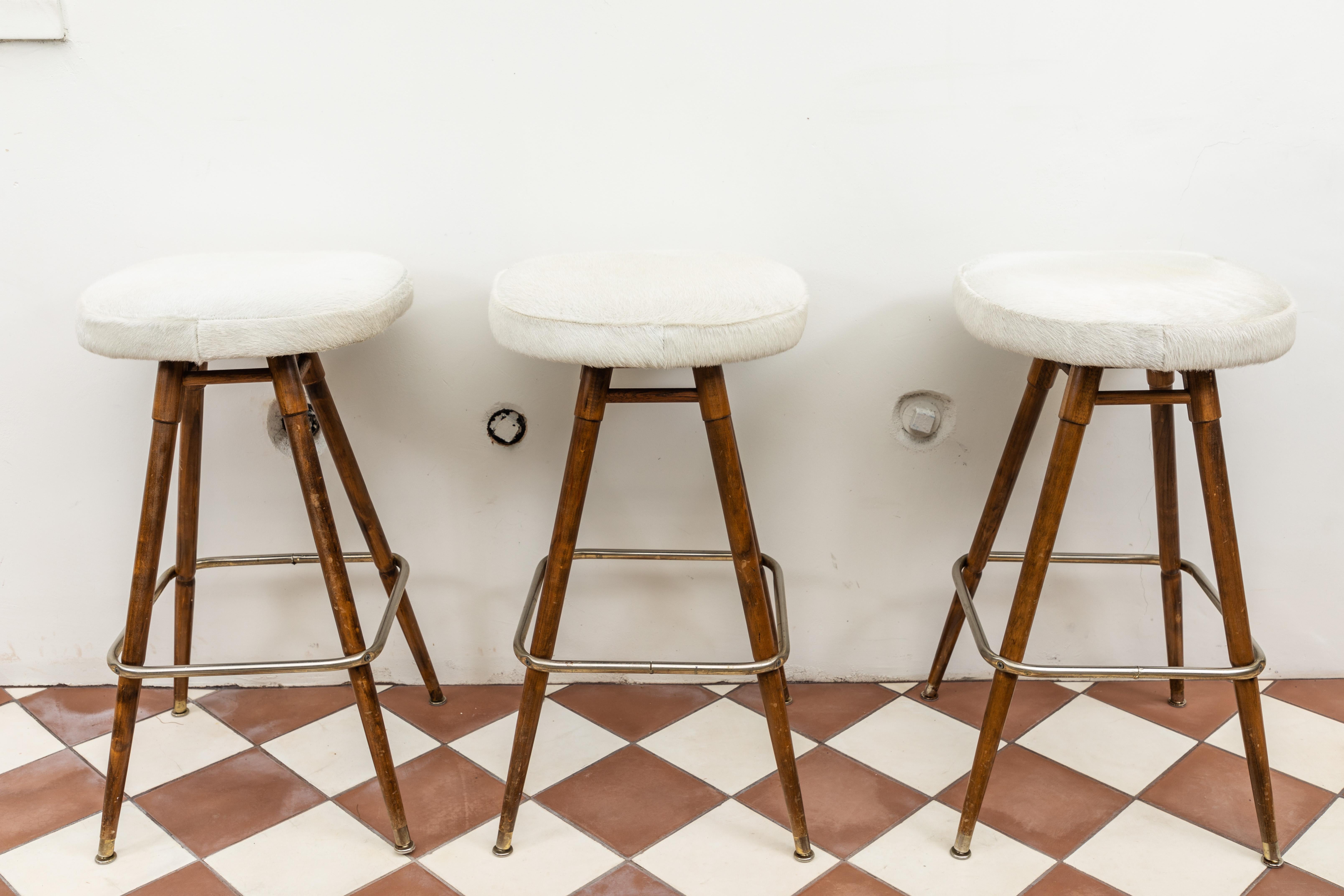 French swiveling bar stools with white hide tops and wood and metal base, circa 1960, set of 3.
