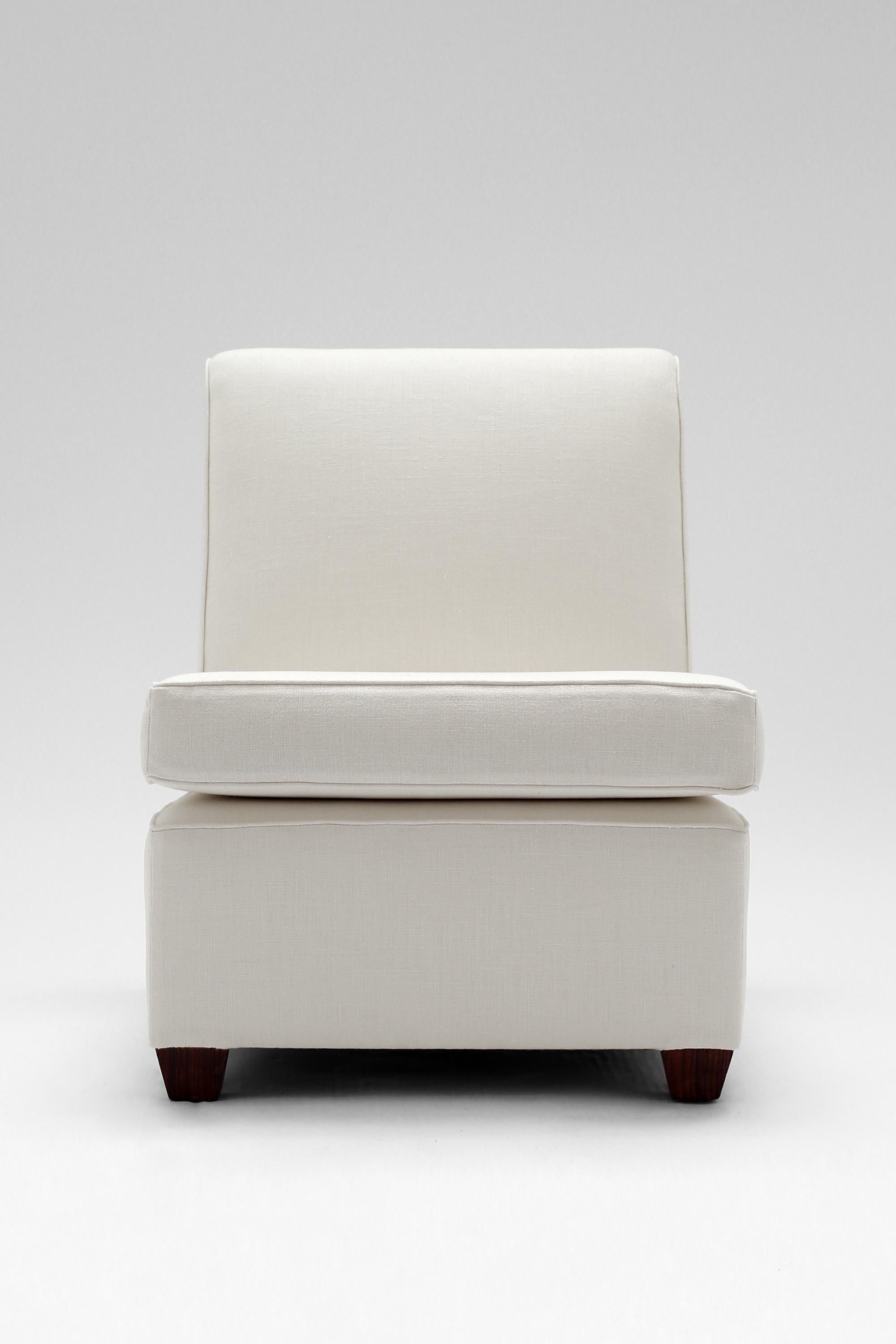 An Art Deco fireside chair or chauffeuse in the manner of Jacques Adnet. Featuring a double sprung seat and block feet veneered in Macassar. Rebuilt and newly reupholstered in white linen. French, c. 1940.