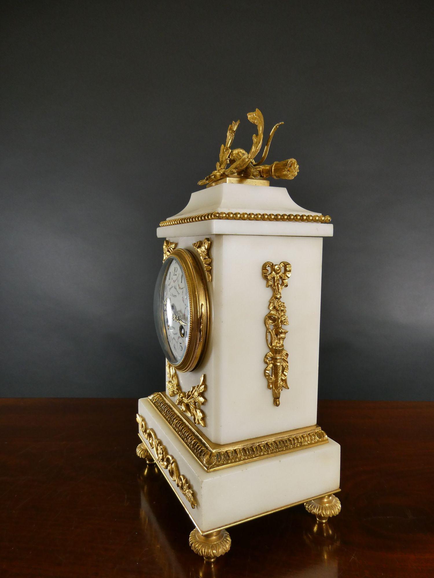 Pendule de cheminée en marbre blanc et bronze doré de Samuel Marti.
 
Boîtier en marbre blanc à socle surélevé avec des montures en bronze doré et un décor de perles surmonté d'une couronne en bronze doré, reposant sur des pieds décoratifs en