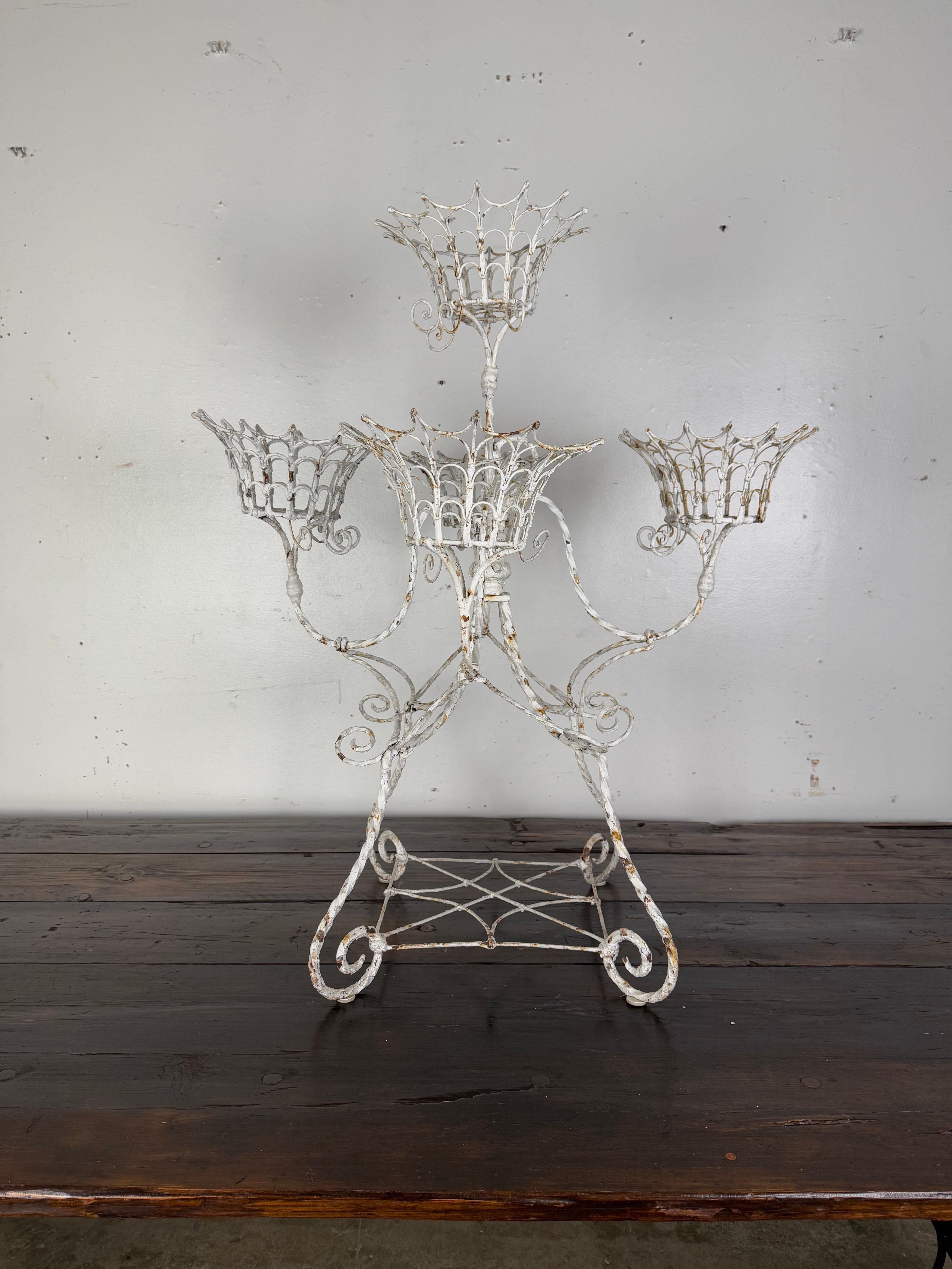 Schmiedeeiserner Pflanzkübel aus Metall im Vintage-Stil mit kunstvollem, dekorativem Design.  Die korbähnlichen Halterungen sind symmetrisch um einen zentralen Stiel angeordnet, wobei sich eine oben und vier unten um den Stiel herum befinden.  Die