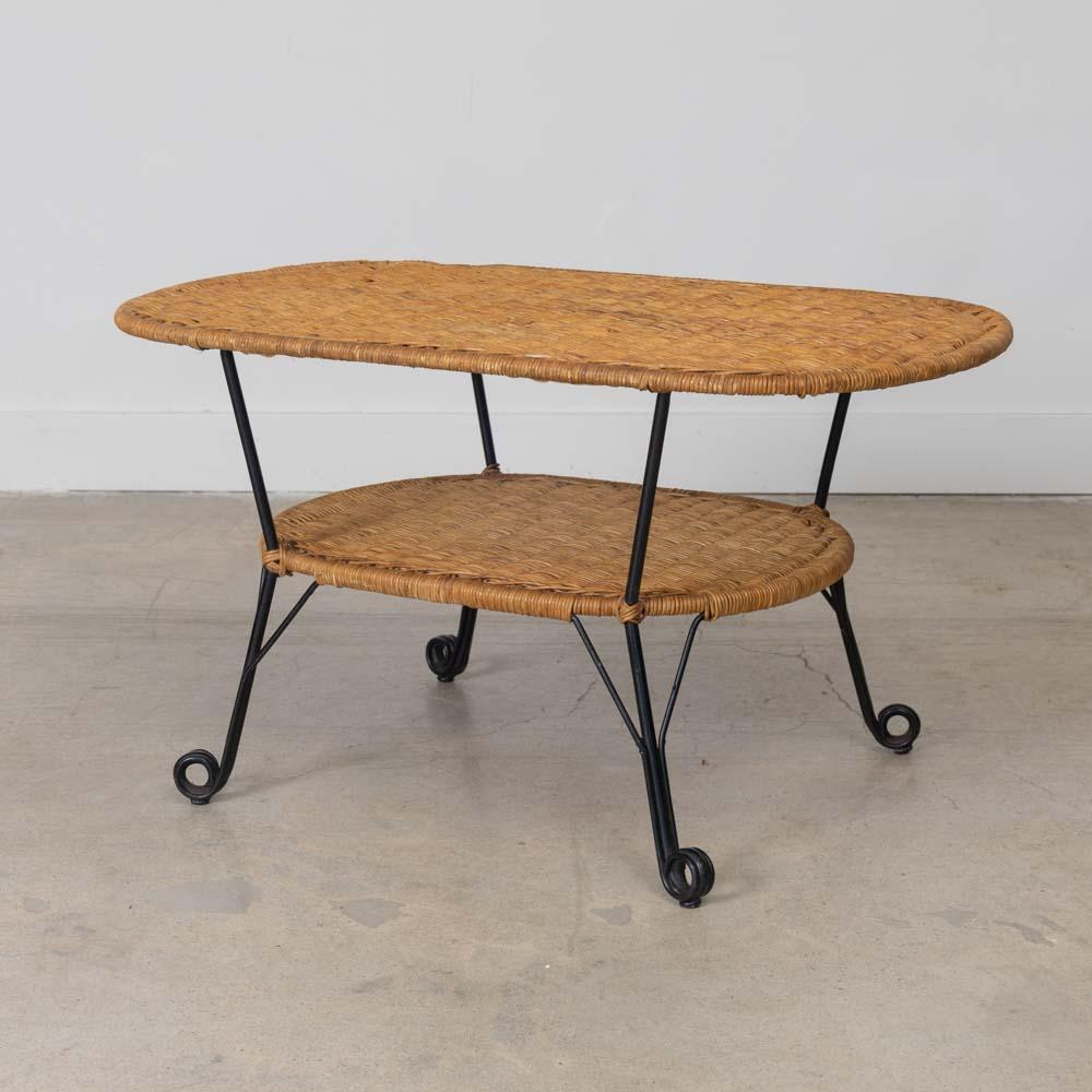 Great oval two-tier wicker and iron coffee table from France, 1950s. Iron frame wrapped in wicker with woven wicker top, lower wicker shelf and lovely looped iron feet. Original wicker and iron show nice age and patina. Functional and unique design. 