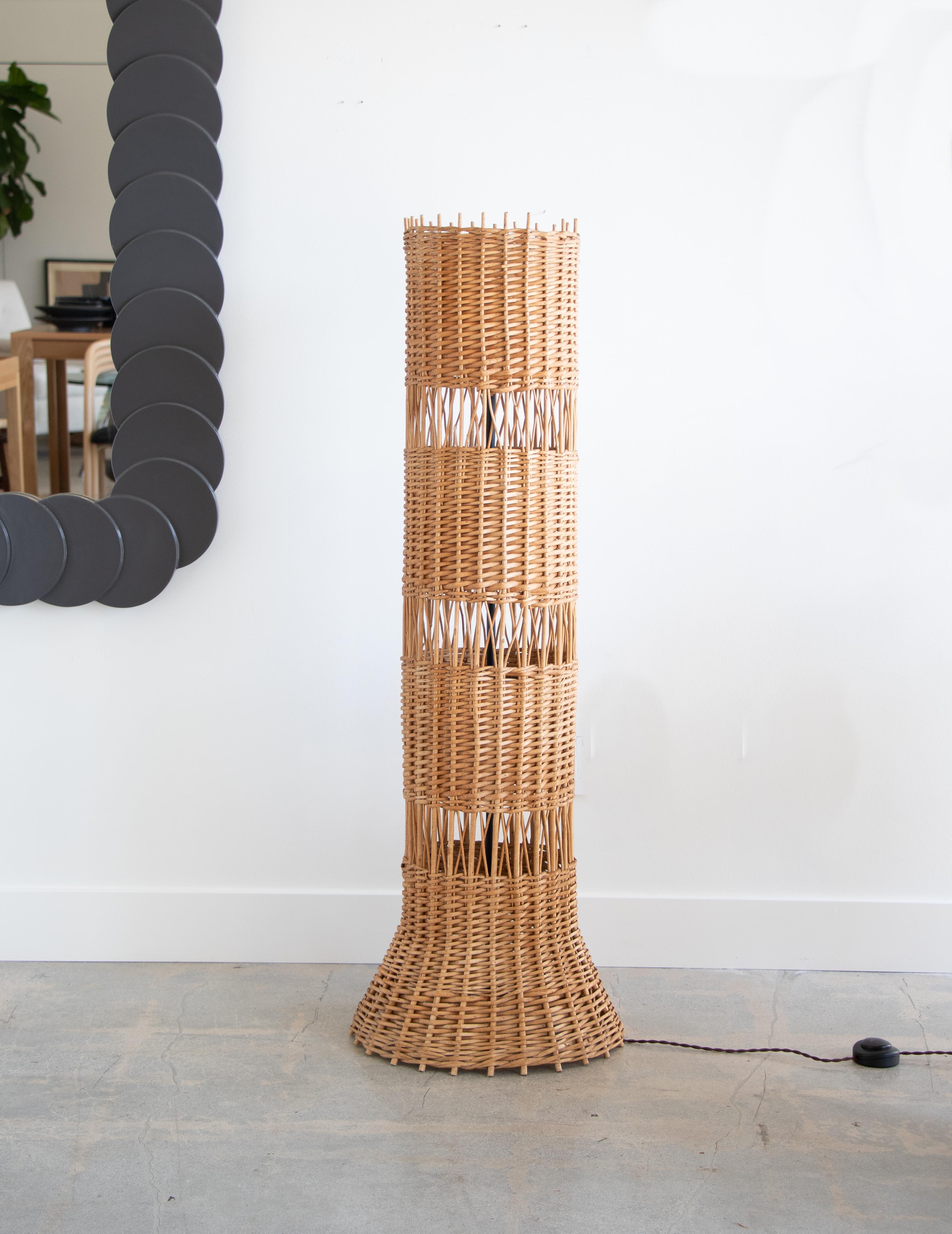 Unique French wicker standing floor lamp in a column shape that measures nearly 4 feet tall. Beautiful woven wicker detail with openings to let the light shine through. Newly made interior black iron stand holds 3 sockets with new wiring. Wicker