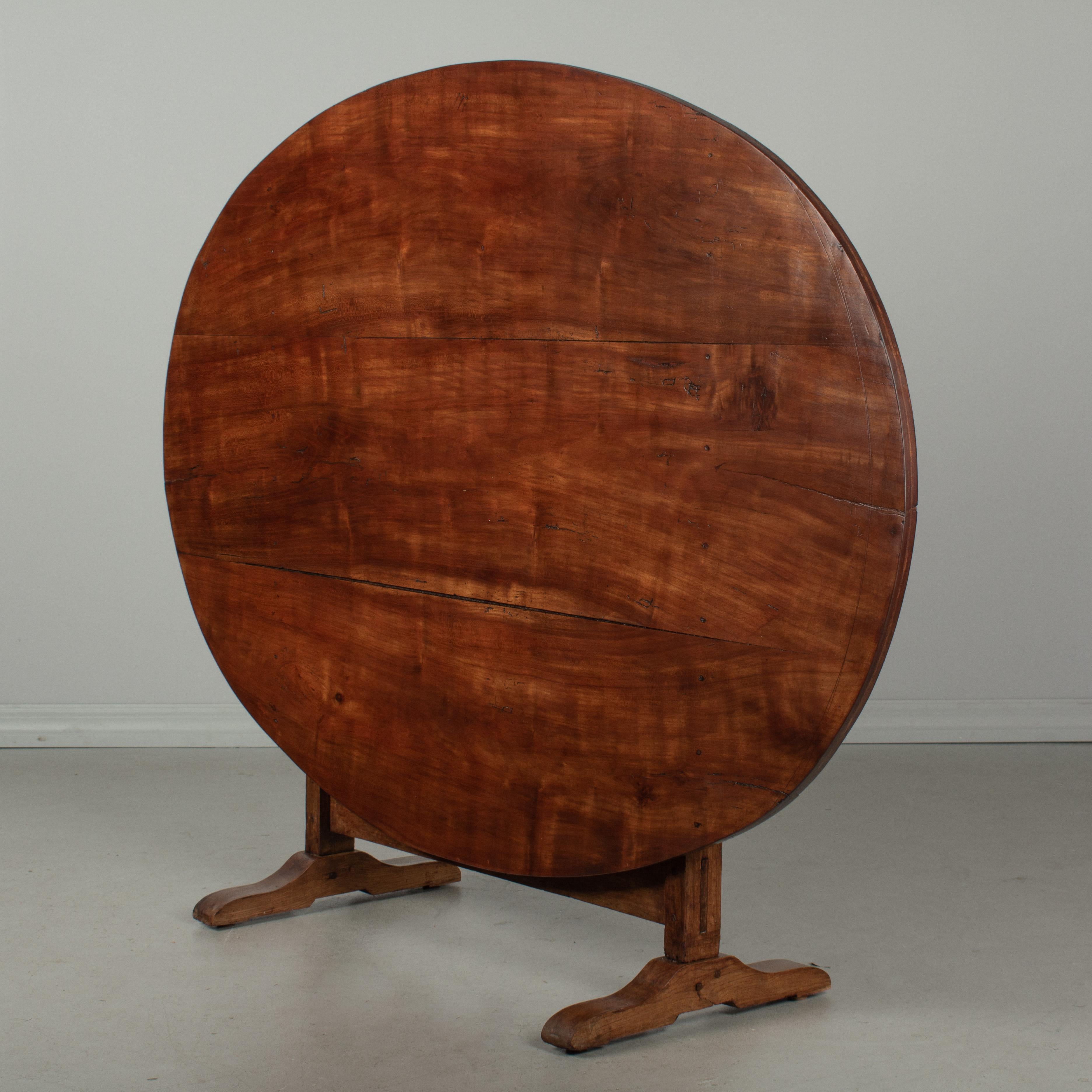 A French wine tasting, or tilt-top table, made of solid cherry. The large oval top is made from three planks of wood and the base is sturdy and well-crafted with mortise and tenon joints and pegged construction. The table top was once covered in