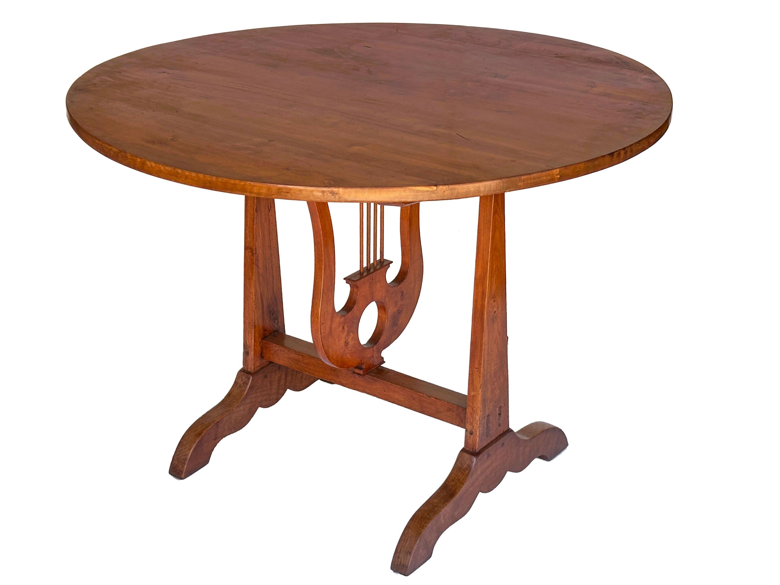 A fine French vendange tilt-top table for wine tasting, circa 1900, featuring a round or circular top of handsomely patinated cherry-wood over a decorative lyre design support. The support arm beneath the table is fashioned into a stringed musical