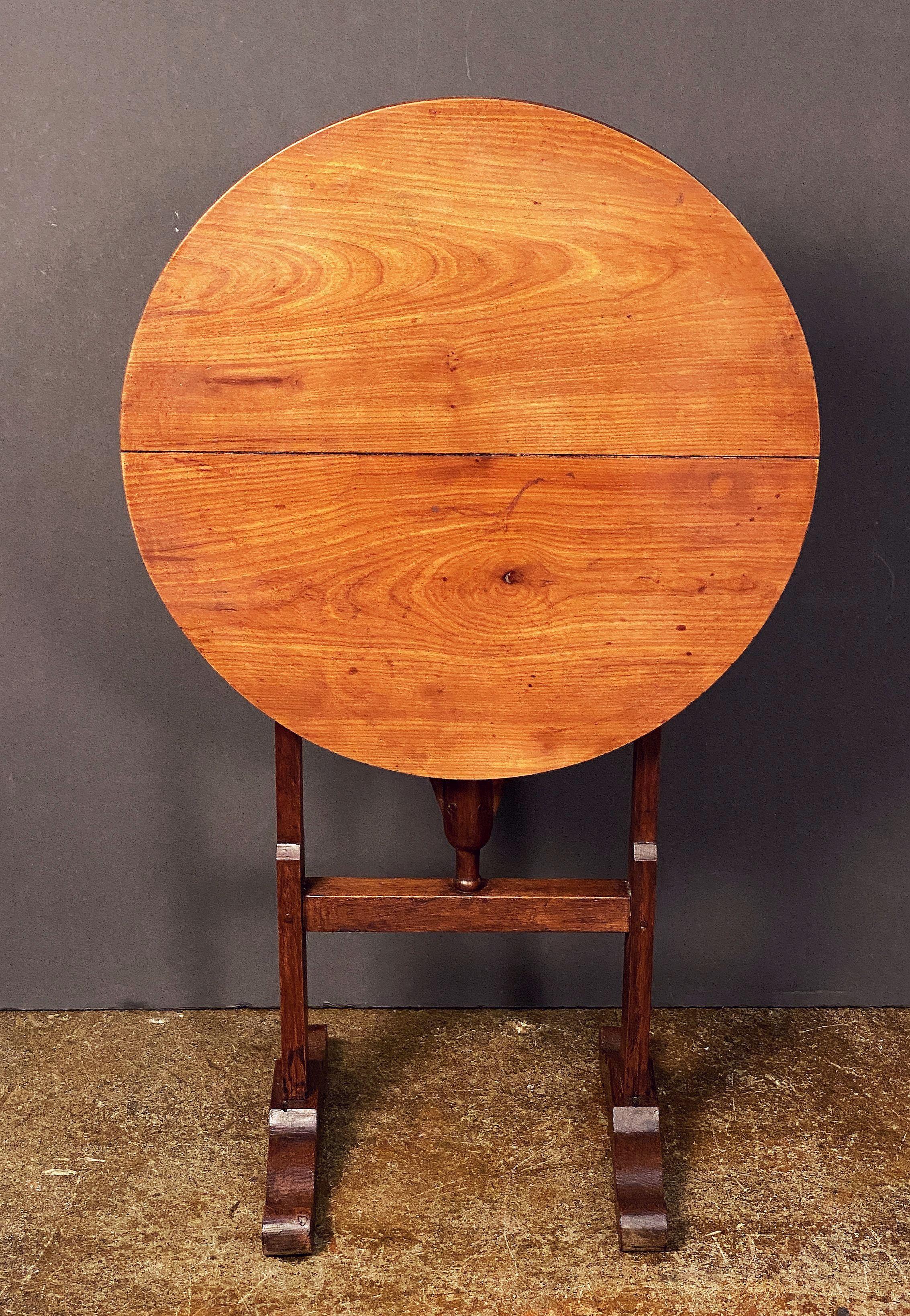 A fine French vendange tilt-top table for wine tasting, featuring a round or circular top of handsomely patinated cherrywood over a stretcher base of chestnut wood.  

Standing height with table tilted in the stowaway position:  35 7/8