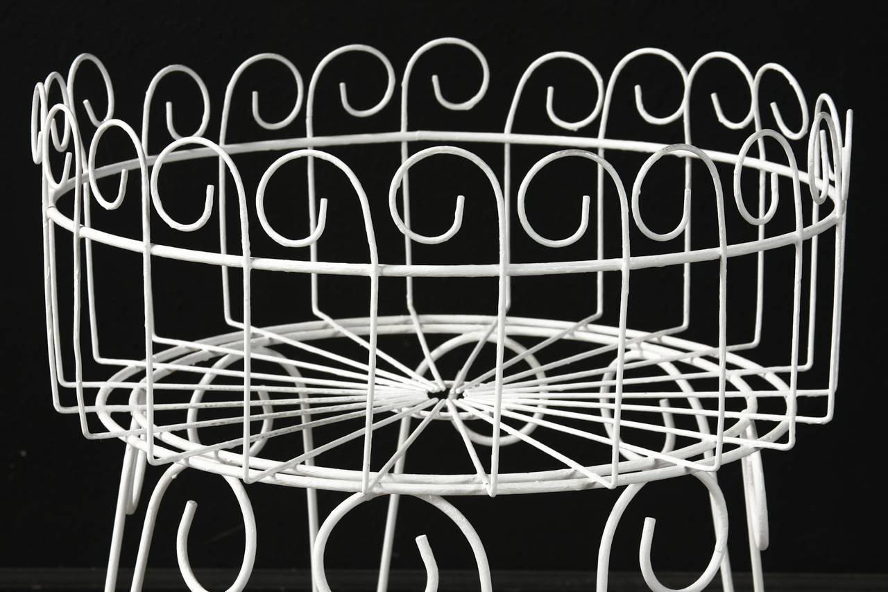 Painted French wire basket plant stand or jardinière with hairpin legs. Features a decorative scrolled motif on top and could serve many purposes. Stable with a flat bottom and round ring stretcher conjoining the legs.
