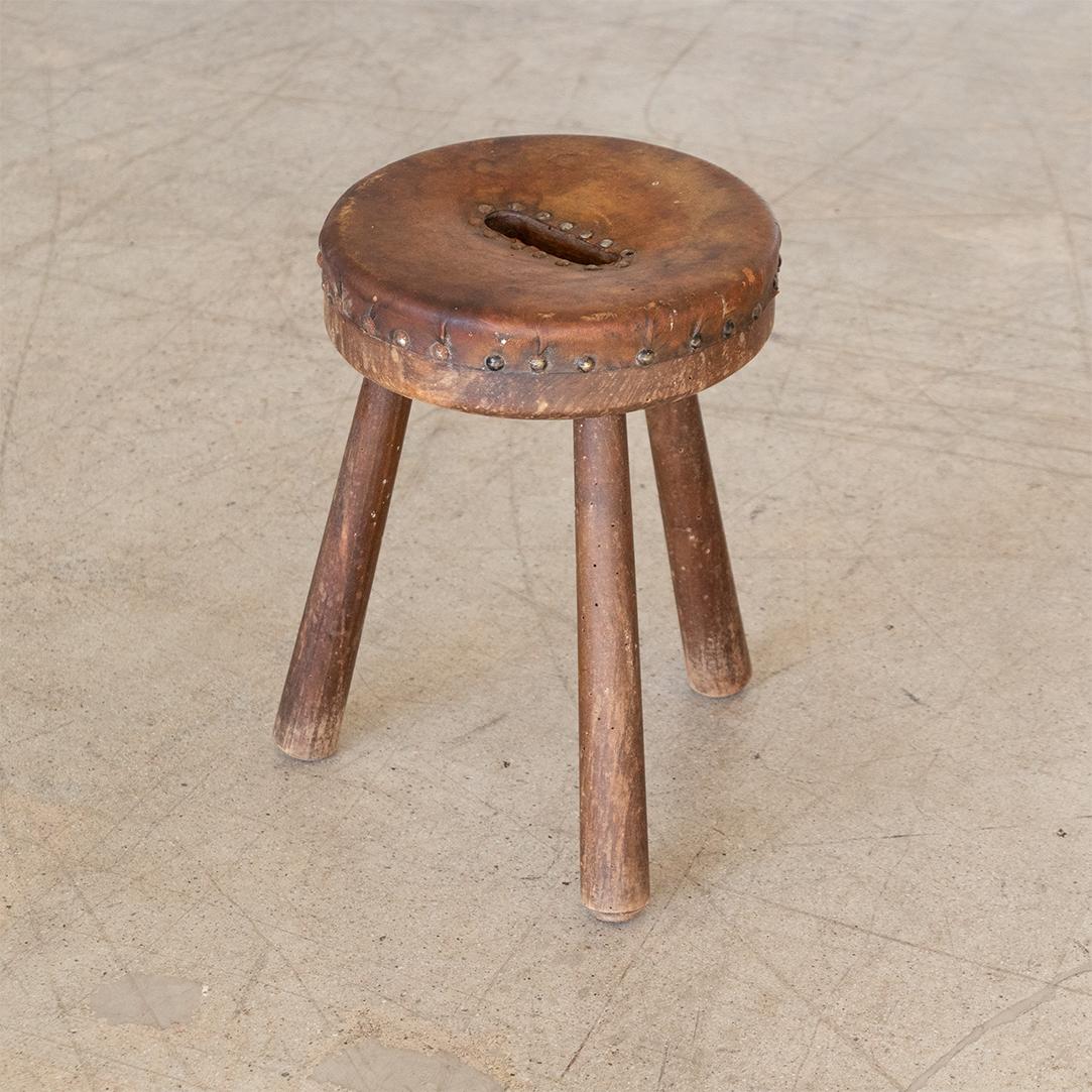 Great wood tripod stool with circular leather seat from France, 1940's. Original dark brown leather seat with nice age and patina. Metal tacks add detail around edge and center hole makes it easy to pick-up and carry. Wonderful age and patina
