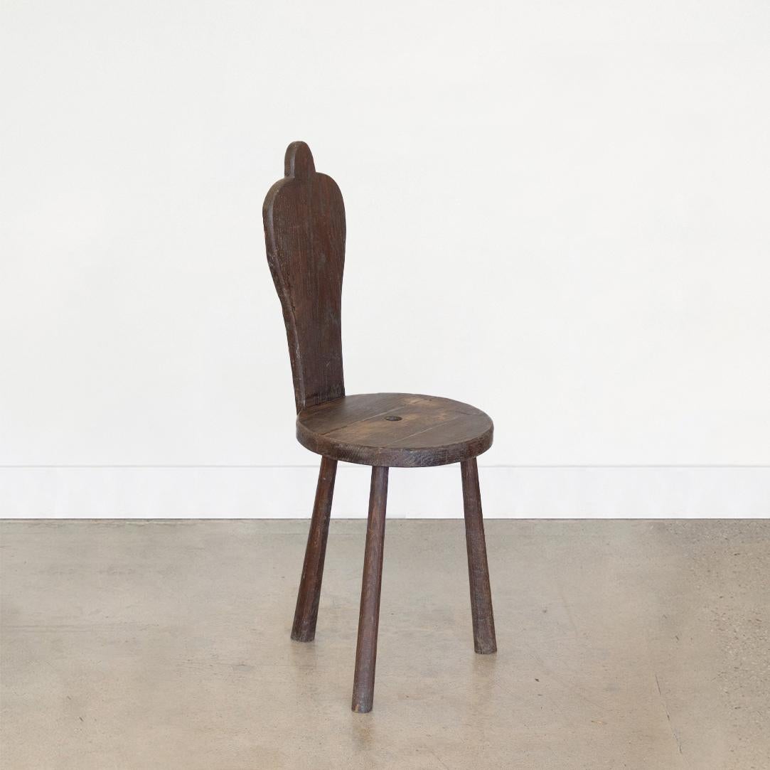 Vintage wood tripod stool from France, 1940's. Three leg wood chair with circular seat and hole detail in center. Slender wood back with decorative carved detail. All original finish showing great age, patina, and wear.