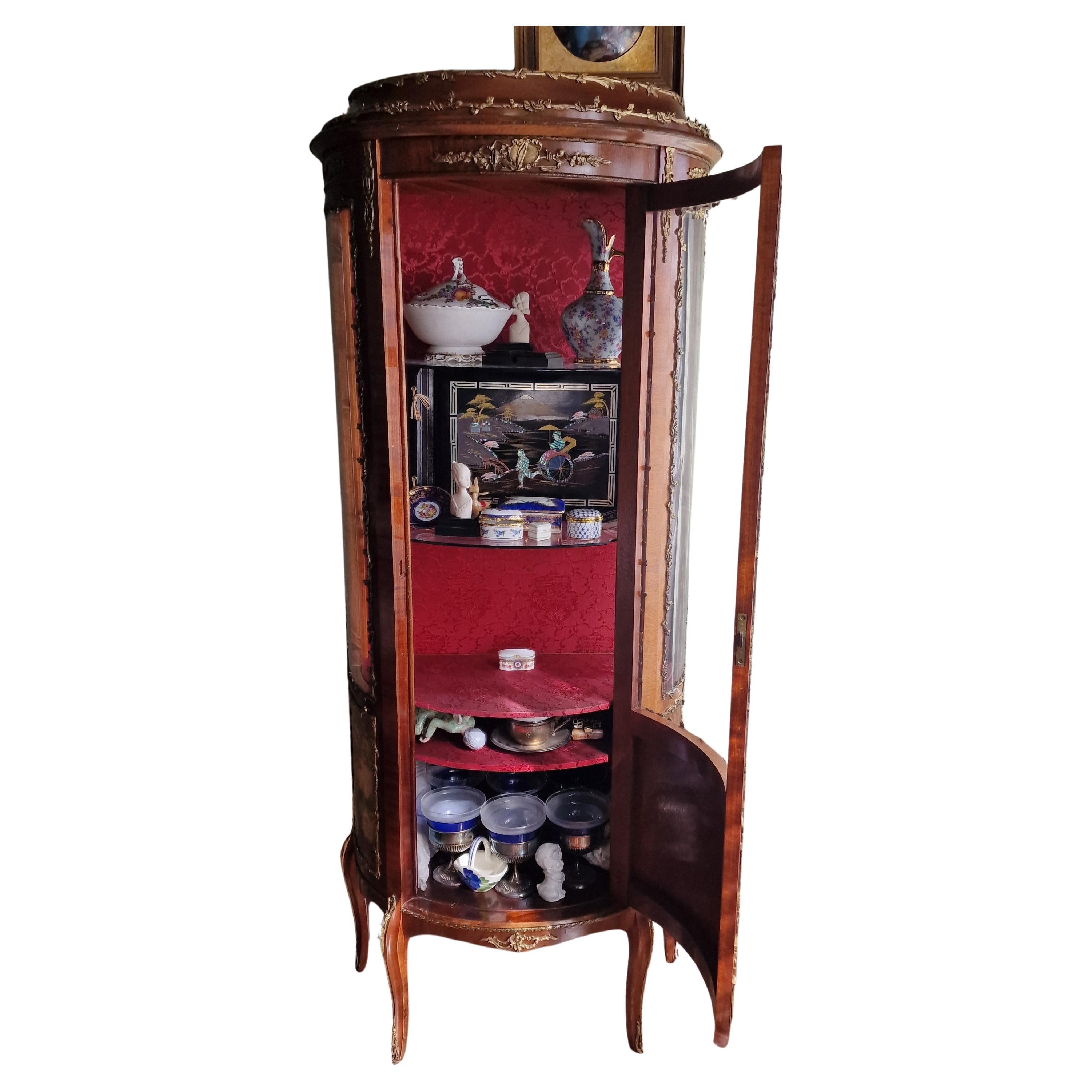 Superbe vitrine semi-circulaire en bois de style Napoléon III, inspirée du Vernis Martin, avec trois panneaux vitrés et trois registres intérieurs. La porte présente une peinture à l'huile sur bois avec une scène classique et académique, flanquée de