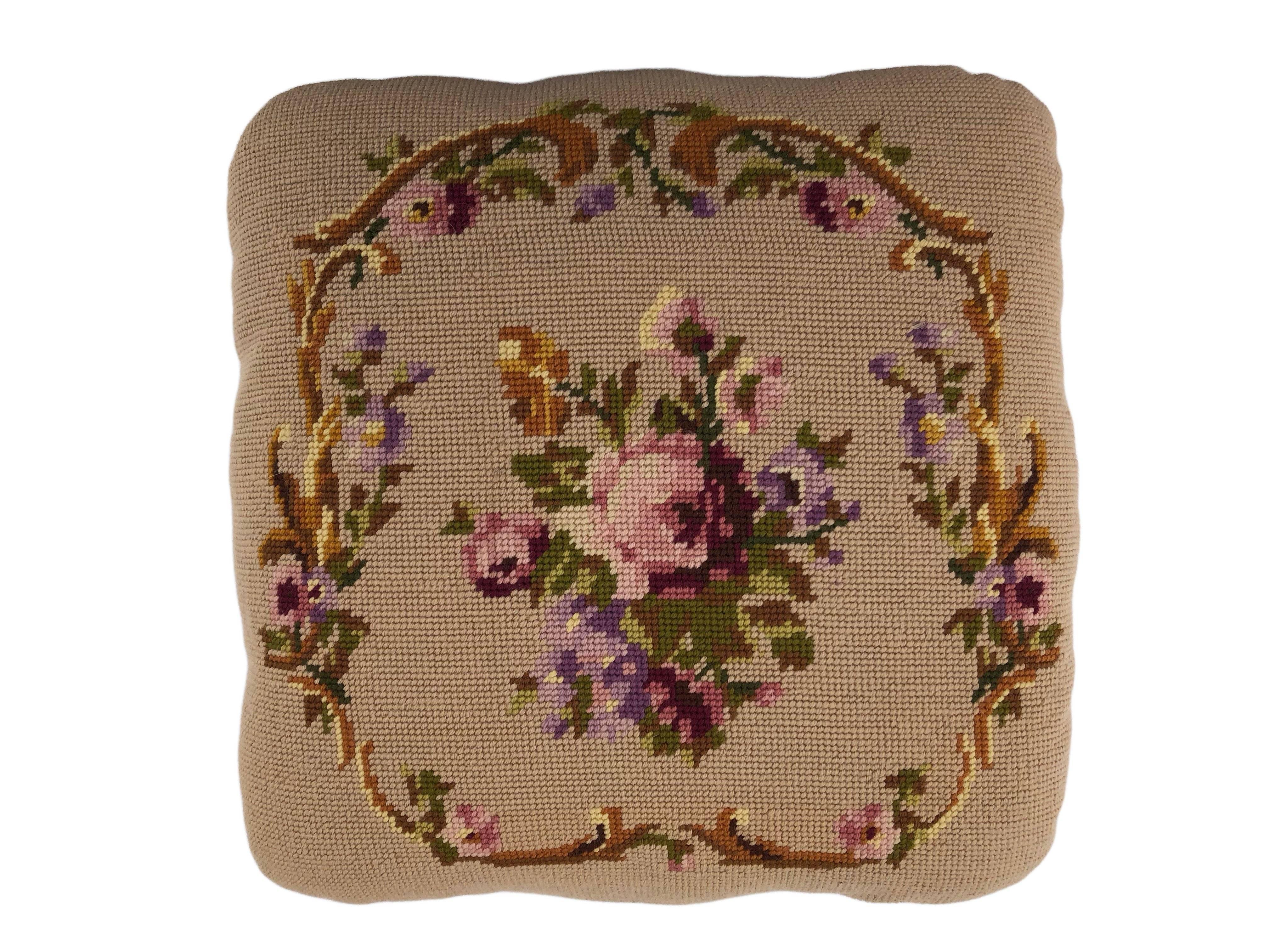 This is a lovely French wood foot stool with a tan/cream background and a beautiful floral embroidery in the centre which is surrounded by a circle of embroidered flowers with a scroll design. The embroidery has beautiful purple, pink, cream, tan,
