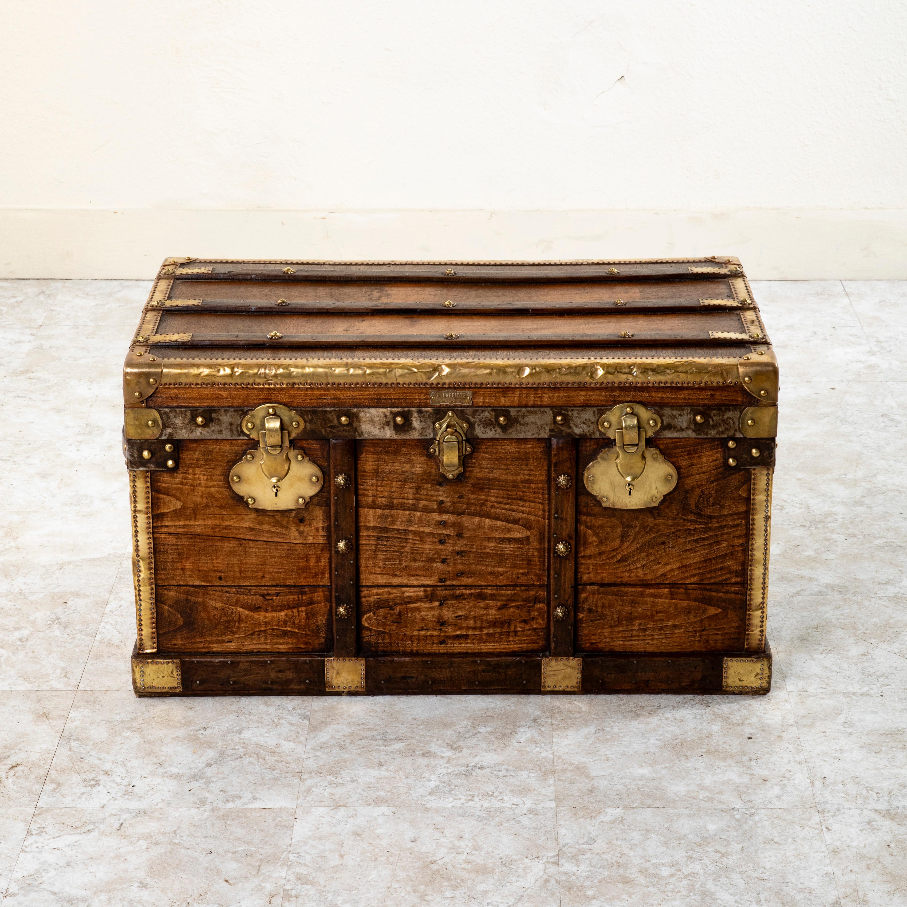 This French wooden steam trunk from the late nineteenth century features locks stamped by the maker, Laffitte, and its address in Bordeaux, 19 Rue Esprits des Lois. Its wooden runners with brass florette rivets and brass corners offered protection