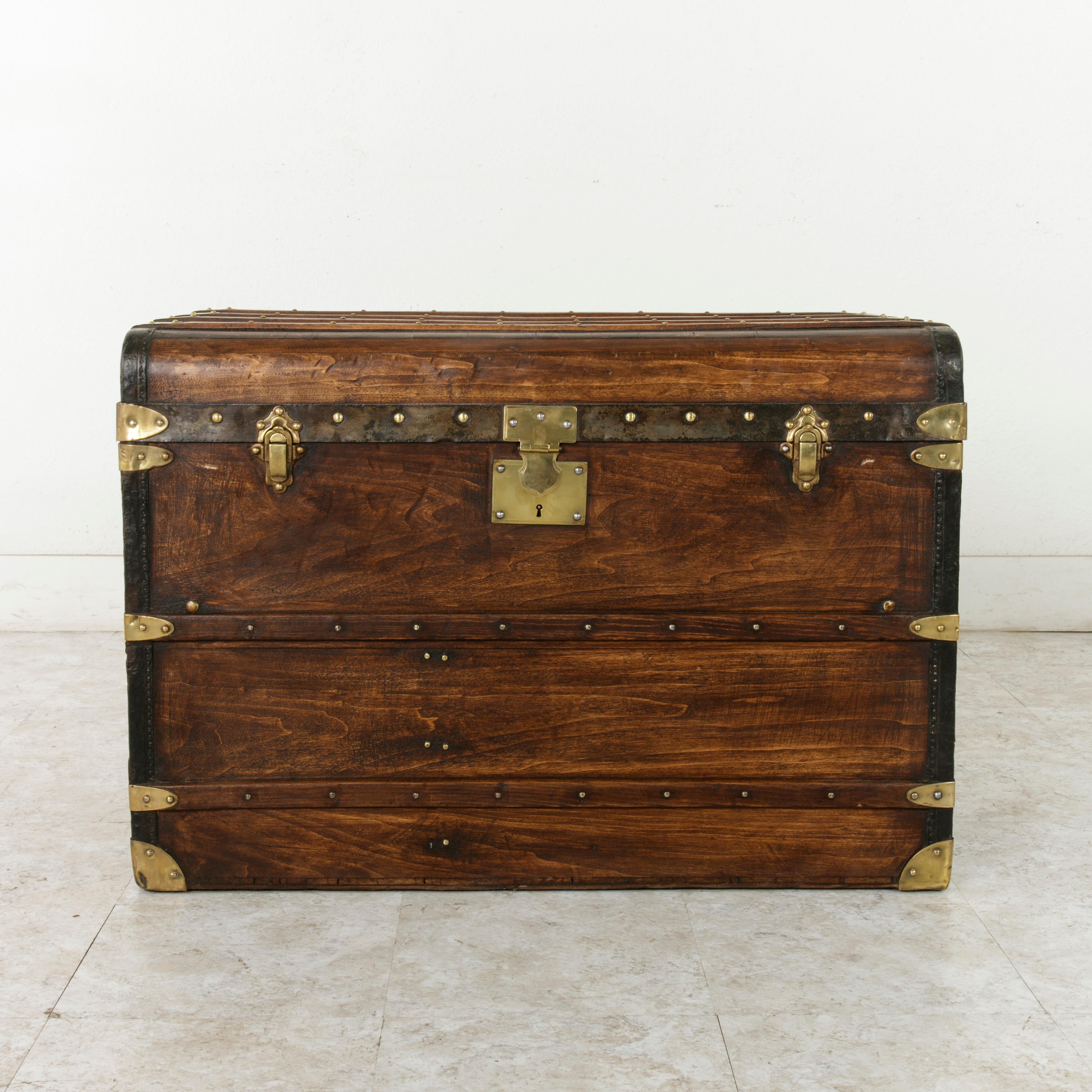 This French wooden steam trunk from the turn of the 20th century features a patch on the back marked Autobus Stock, Neris-les-Bains, Correspondance du P.O. This patch indicates the trunk's use later in the century for bus transportation in the
