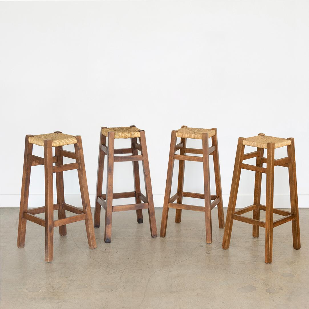 Set of four rustic wood bar stools from France, 1940's. Dark wood frame with foot rests and light woven rush seat in original condition. Sold as a set. 

Seat measures 10.5