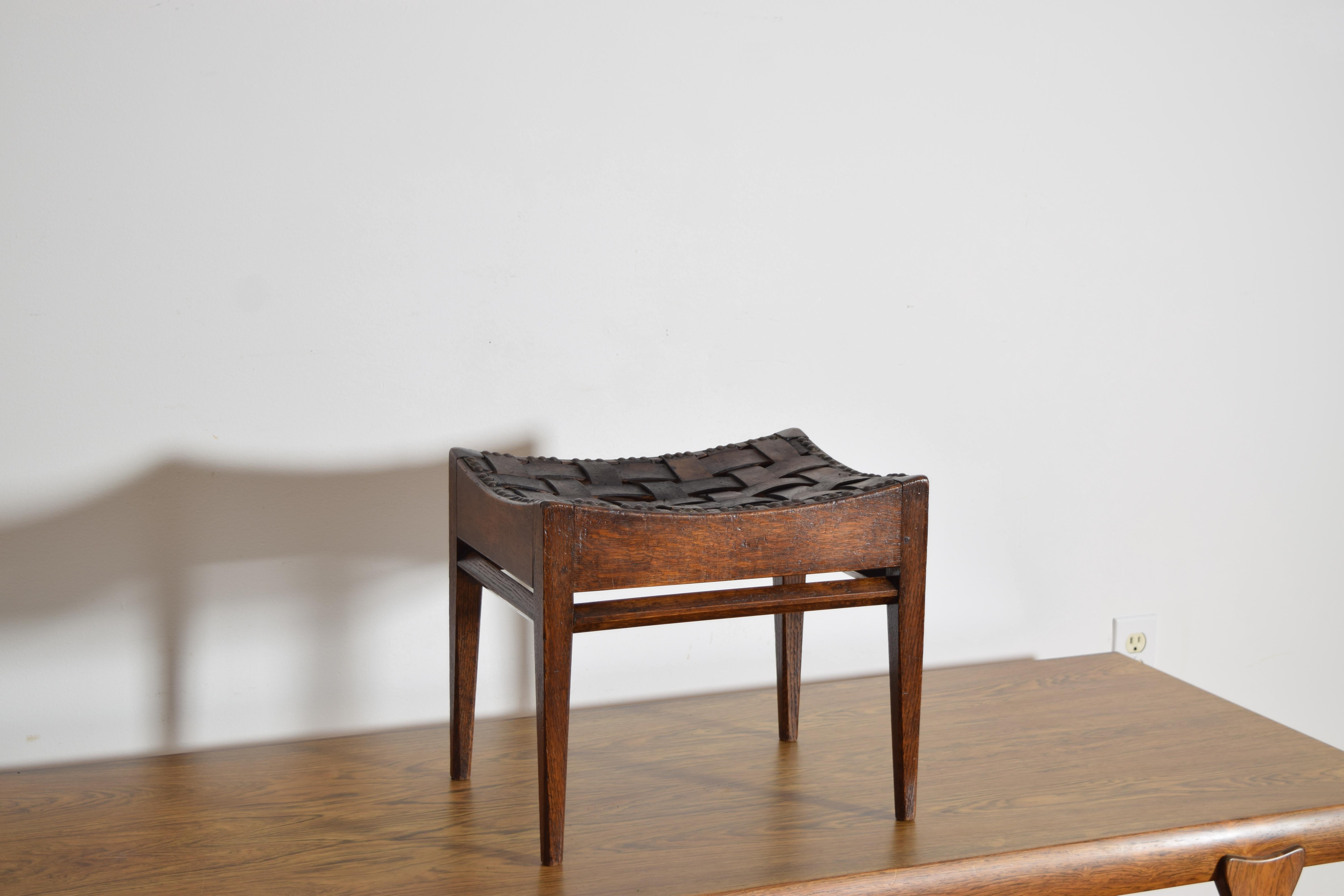 having a concave shaped top with a woven leather seat held in place by patinated brass nailheads, with a high 4-sided stretcher and raised on tapering legs