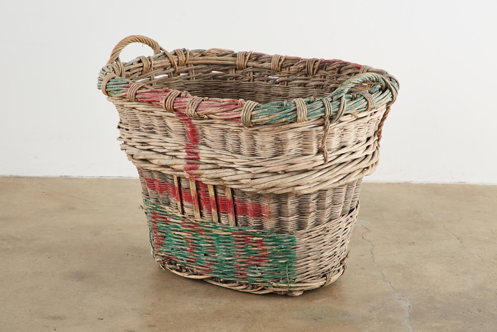 Rustic French chateau champagne grape harvesting basket constructed from woven wicker reeds. Features a thick braided top with handles on each end and brightly colored champagne house initials on the sides reading E.D.P in vivid red and green paint.