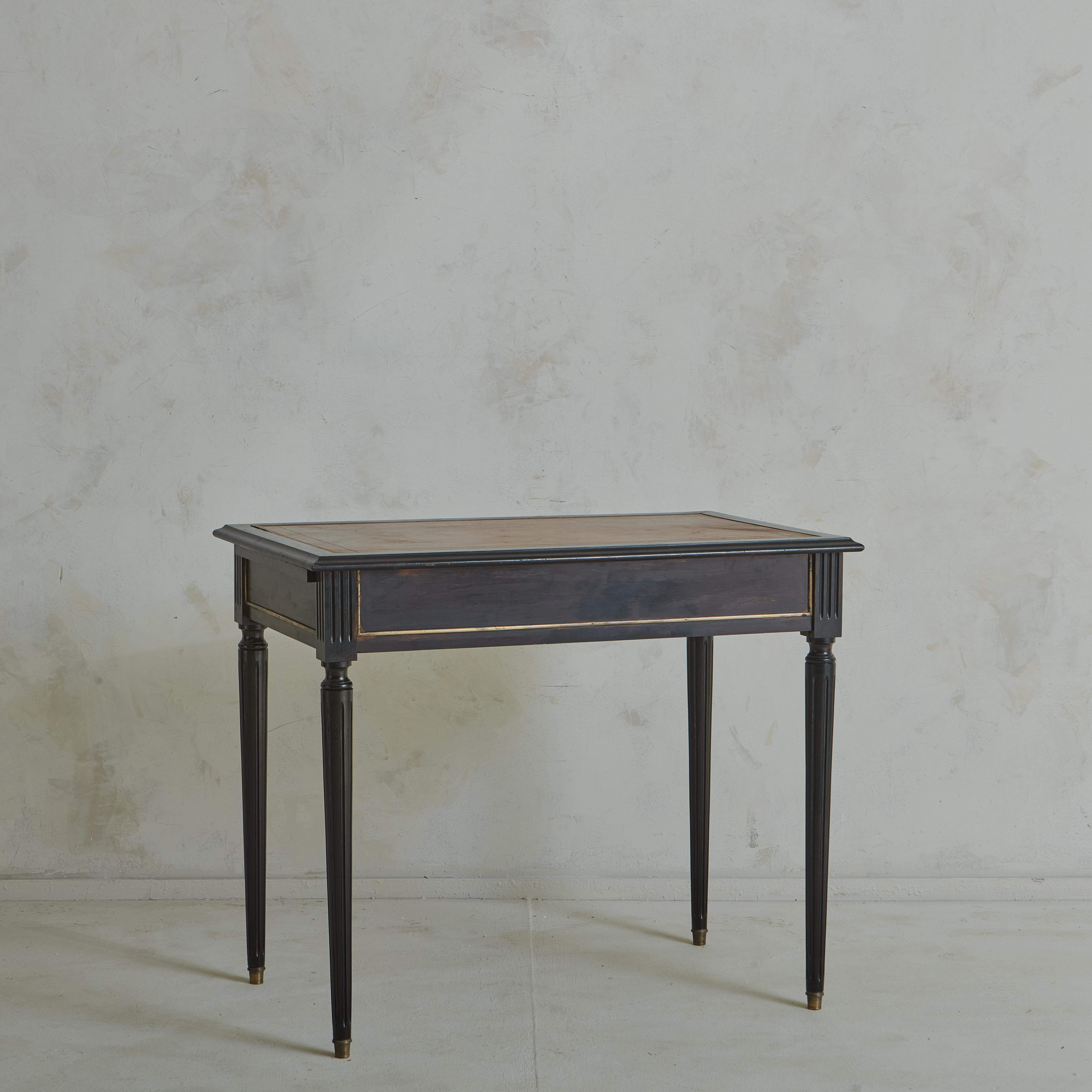 An elegant French Louis XVI style writing desk featuring an inset, embossed chestnut brown leather top with a hand applied gold leaf trim. This desk has two extendable leaves, which pull-out from the sides of the desk, providing additional surface