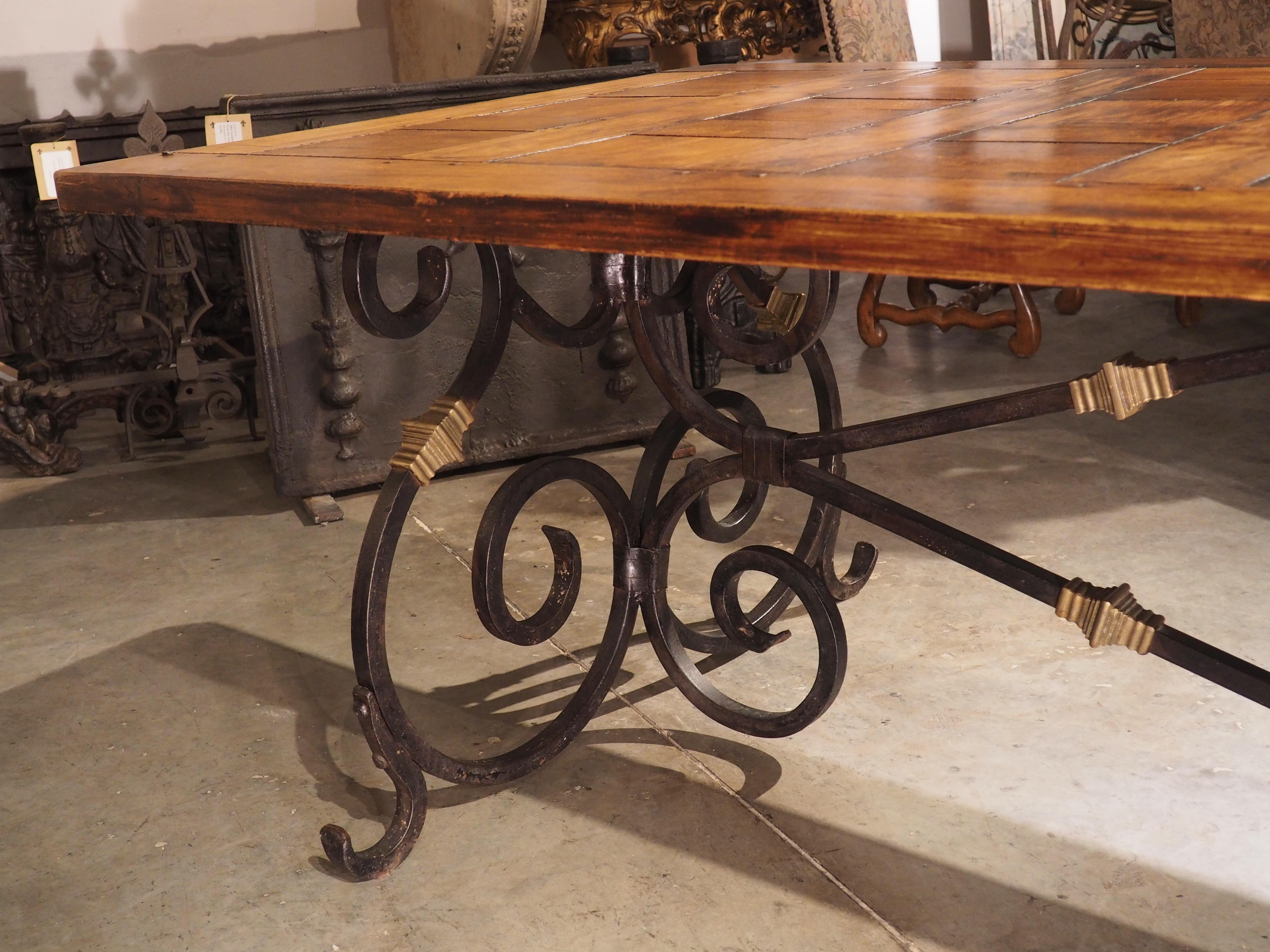 Surmounted by antique parquetry that was constructed using round pegs, this wrought iron and bronze dining table was crafted in France, circa the 1940’s. The top has been laid out in a linear echelle (ladder) parquetry pattern, contrasting with the