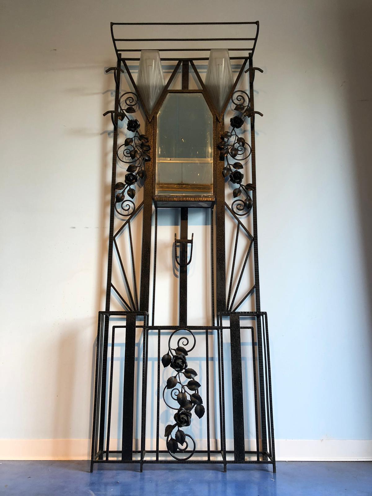 Ravissant portemanteau en fer forgé Art Déco à texture martelée noire, joliment décoré de roses sur les côtés et en bas. Au milieu, un petit miroir avec des lumières. 
France, 1930.