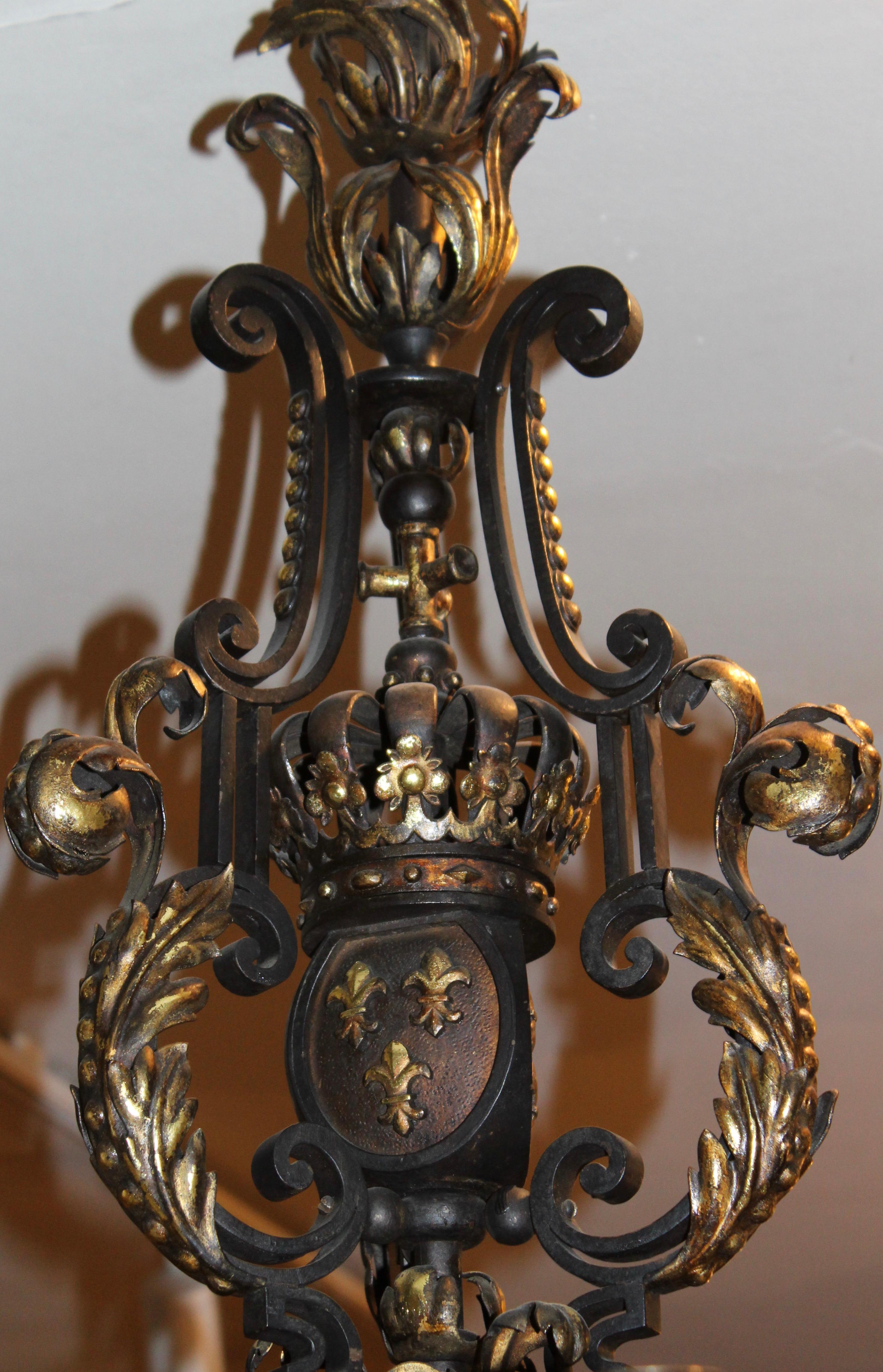 Aufwändig geschmiedeter Kronleuchter aus Eisen aus dem Jahr 1890 mit 6 nicht verdrahteten Armen, verziert mit vergoldeten Fleur-de-Lis-Motiven.
Die Lorbeeren auf dem Blätterdach sind vergoldet, der zentrale Schaft besteht aus einer Königskrone über