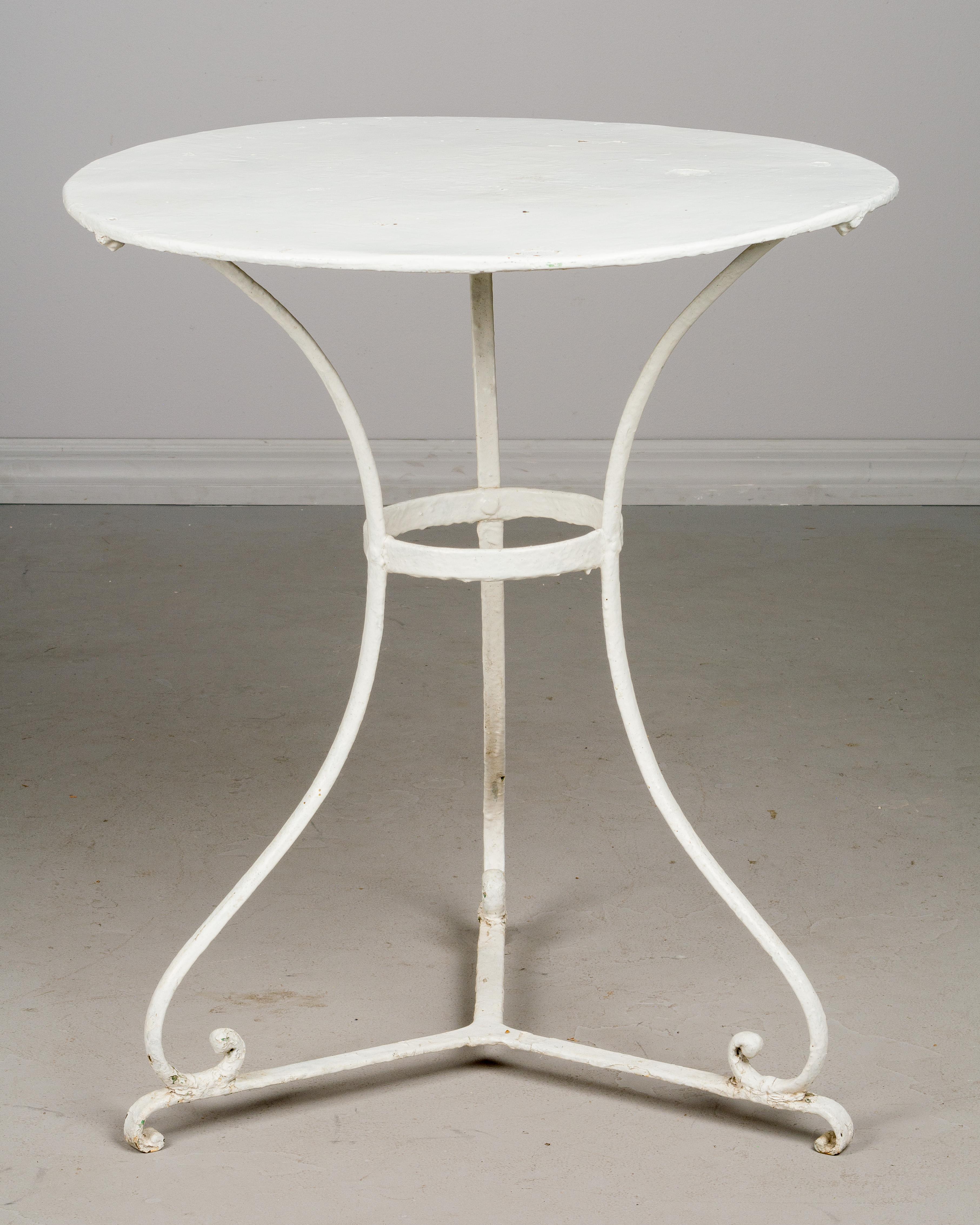 A late 19th century French wrought iron bistro table with old white painted patina and tole top.