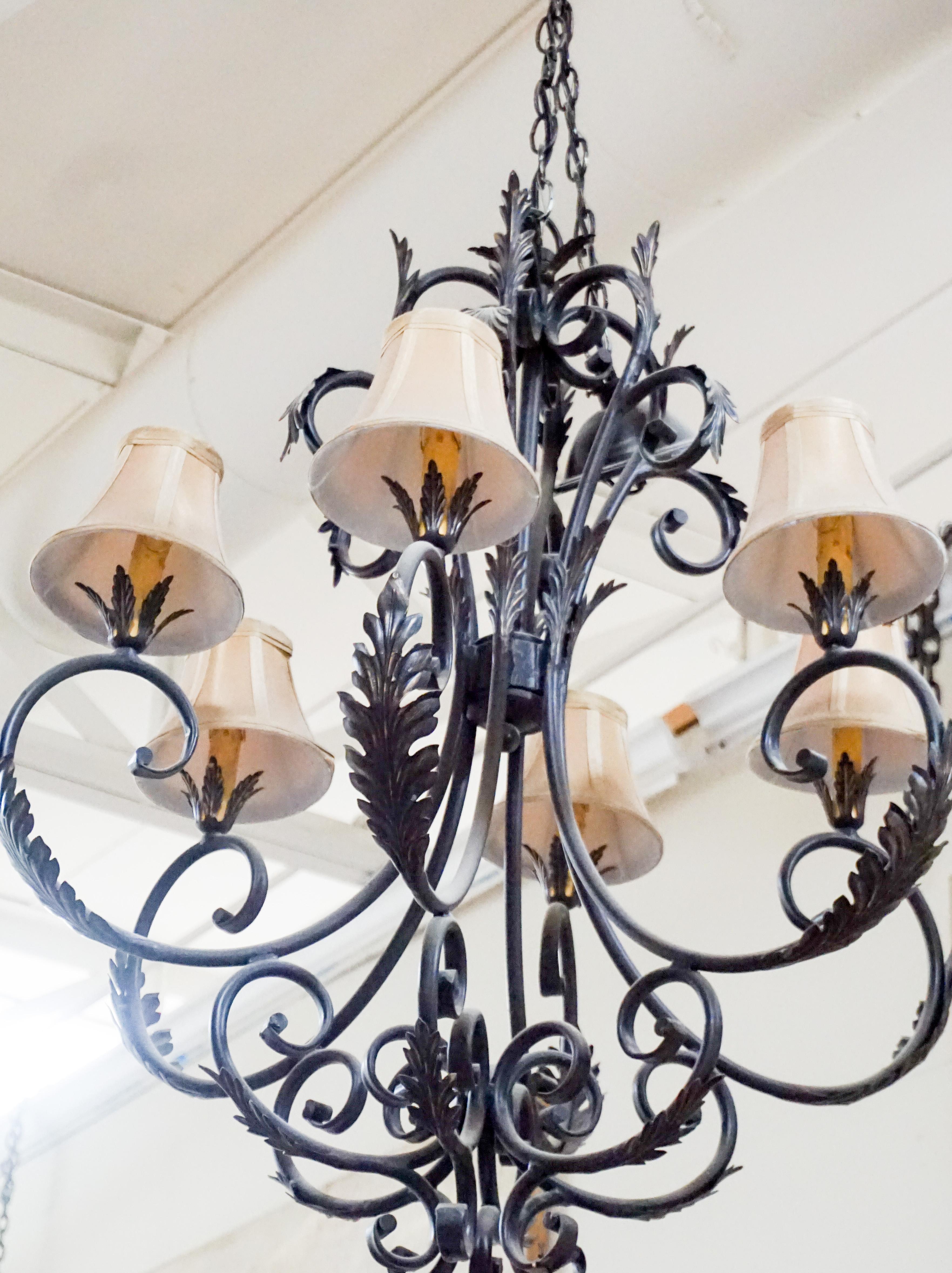 French wrought iron chandelier featuring acanthus leaf decode and 6 arms topped with small shades.