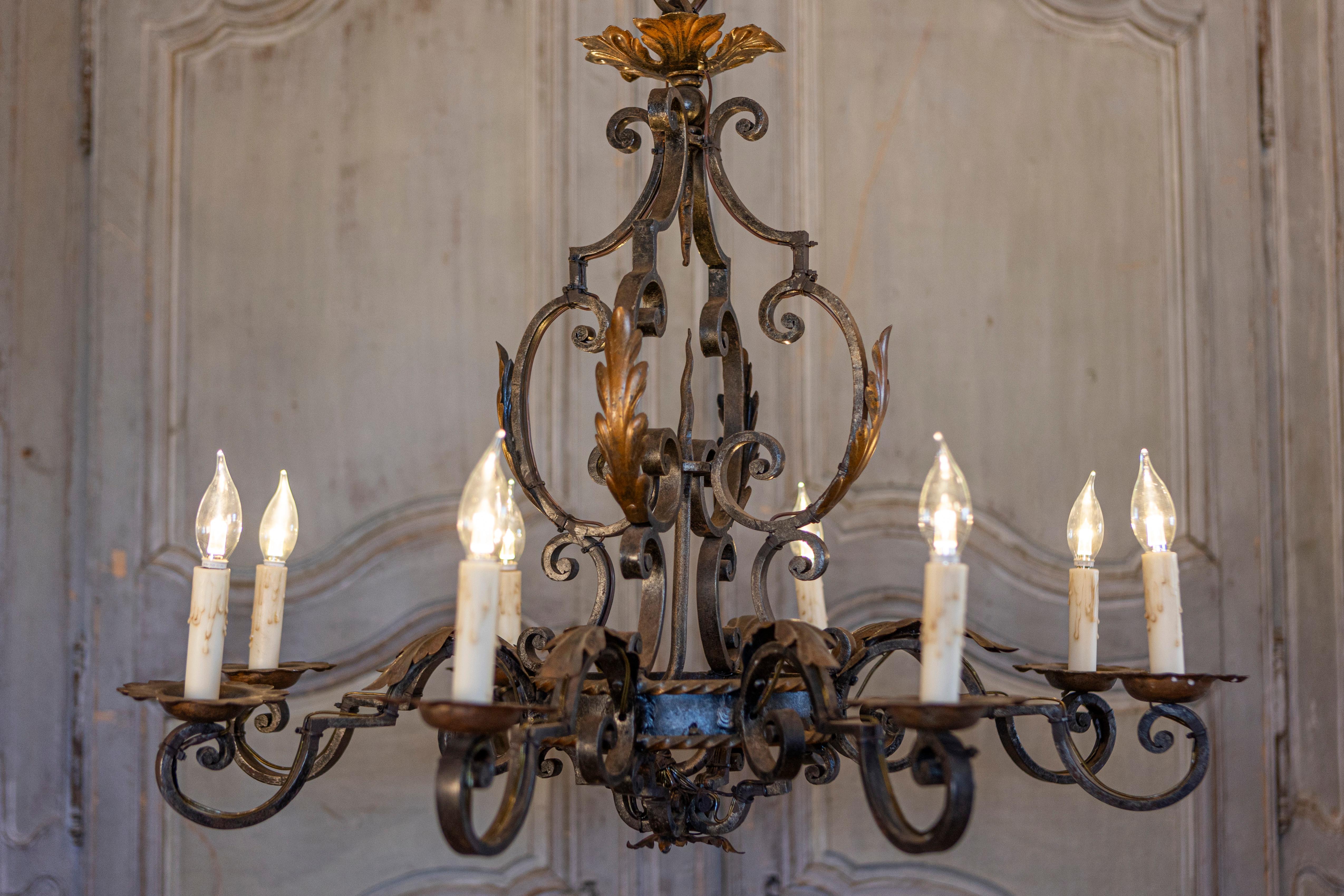 A French wrought iron eight-light chandelier from the 20th century with scrolling arms and acanthus leaf motifs. This captivating French wrought iron chandelier, hailing from the 20th century, serves as a testament to timeless craftsmanship and