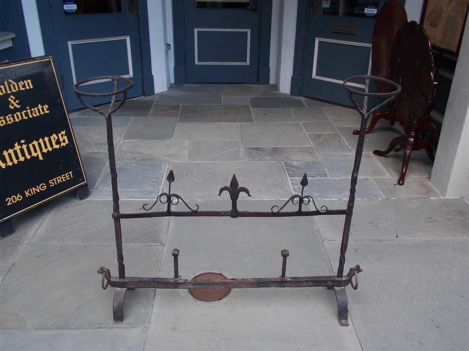 French wrought iron fire place guard with flanking candleholders, spiral columns, scrolled flanking spades with a centered flu-de-lee, two faceted decorative spikes, and terminating on scrolled legs with decorative flanking outer rings. Late 18th