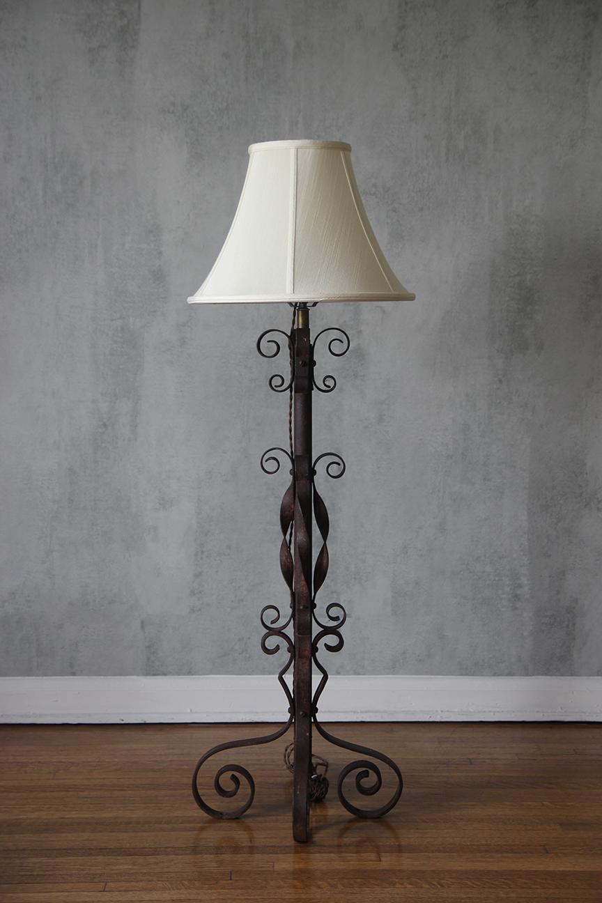 Questa squisita lampada da terra della metà del secolo scorso è uno splendido esempio di artigianato francese, prodotto negli anni '40. Realizzata in ferro forgiato nero, la lampada è caratterizzata da splendide volute rifinite in tonalità rame