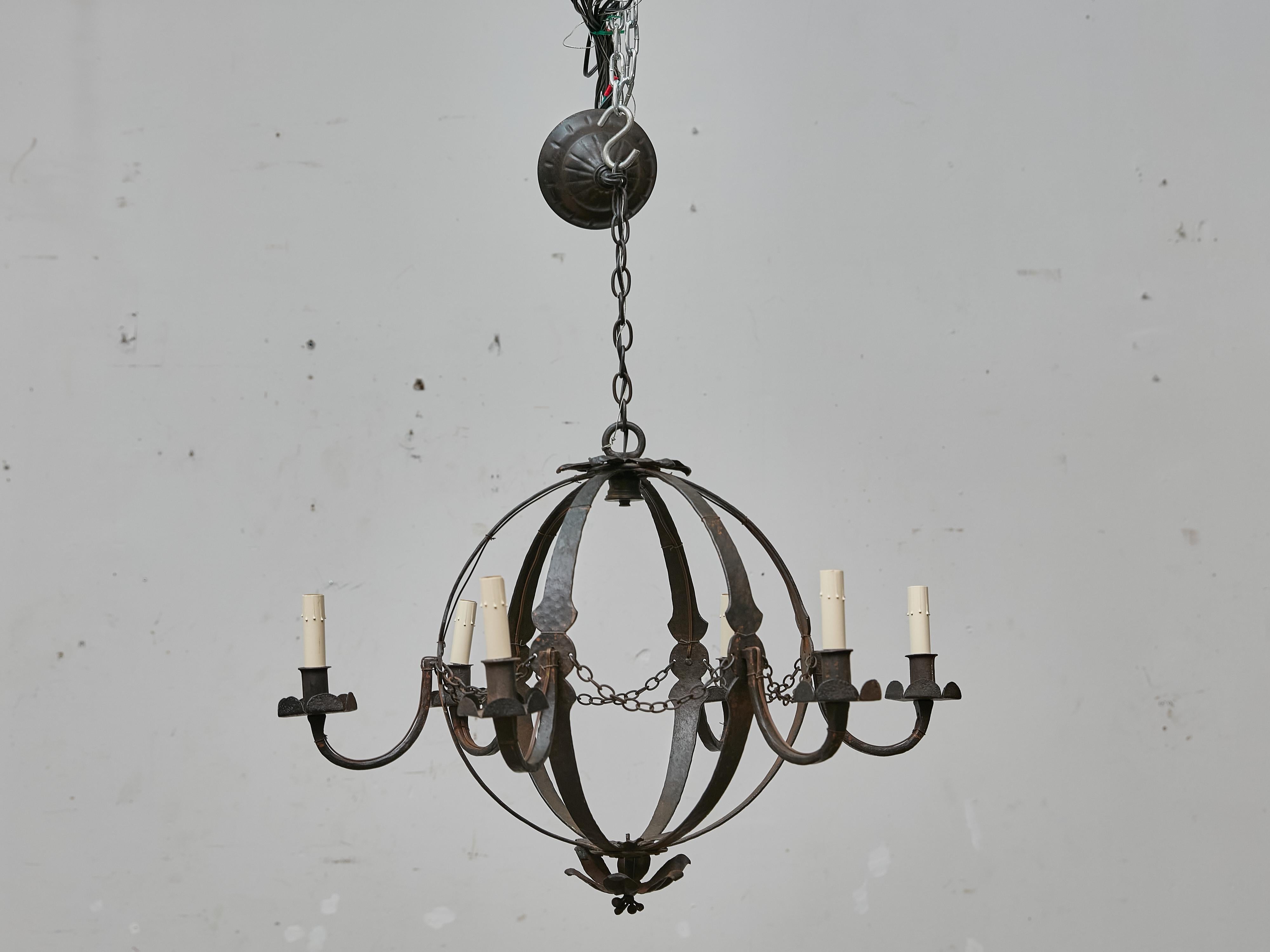 Questo antico lampadario francese, realizzato nel 1900 circa, mostra la presenza audace e l'eleganza duratura del ferro battuto forgiato a mano. Progettato con una forma sferica o a globo, il lampadario è costruito da sei fasce di ferro sagomate che