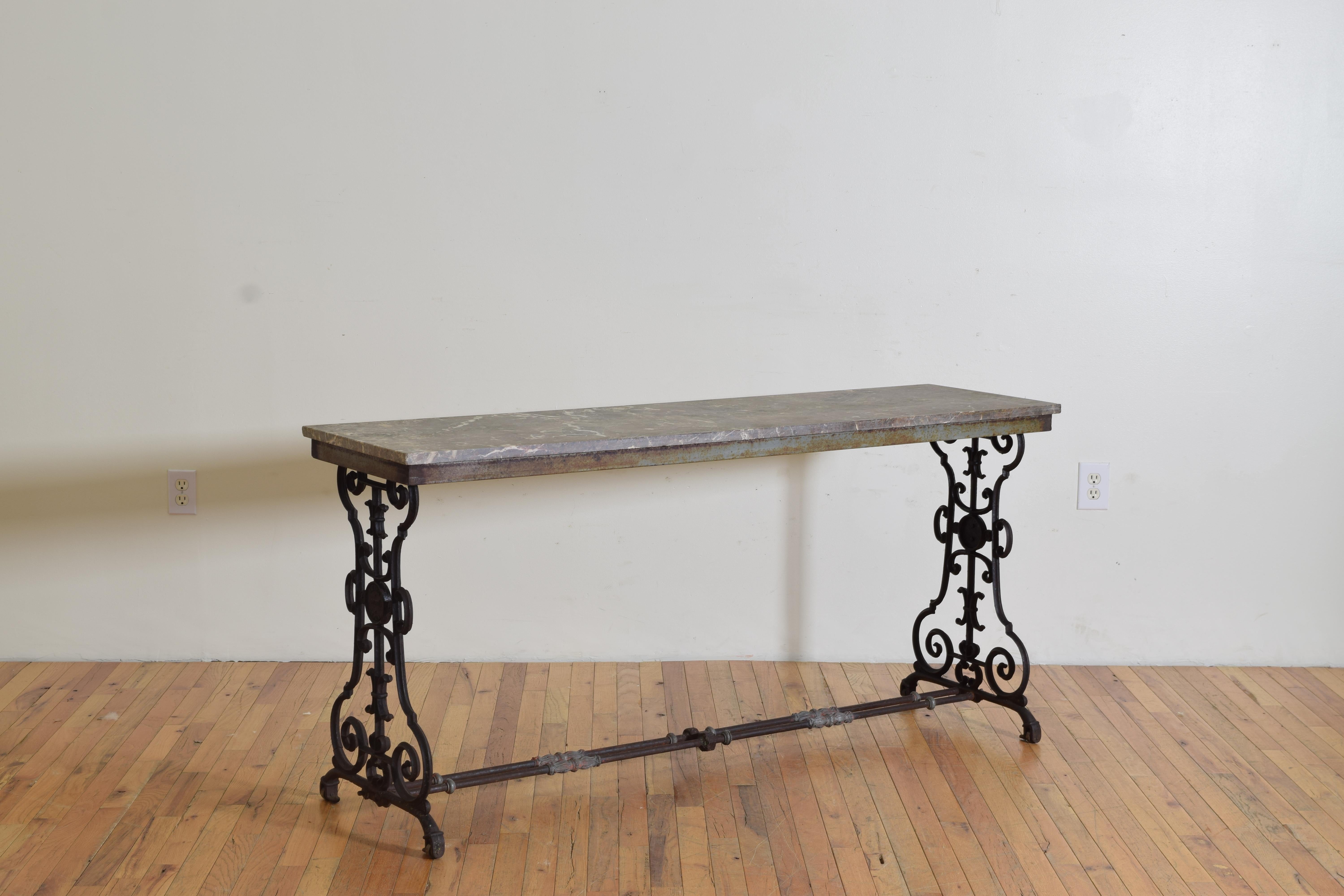 Dieser Tisch mit seiner scheinbar originalen Marmorplatte ist von Hand aus Schmiedeeisen gefertigt und besteht aus einer Reihe von C-Rollen in und um zwei urnenförmige Stützen, die durch zwei Stangen als Strecker verbunden sind.