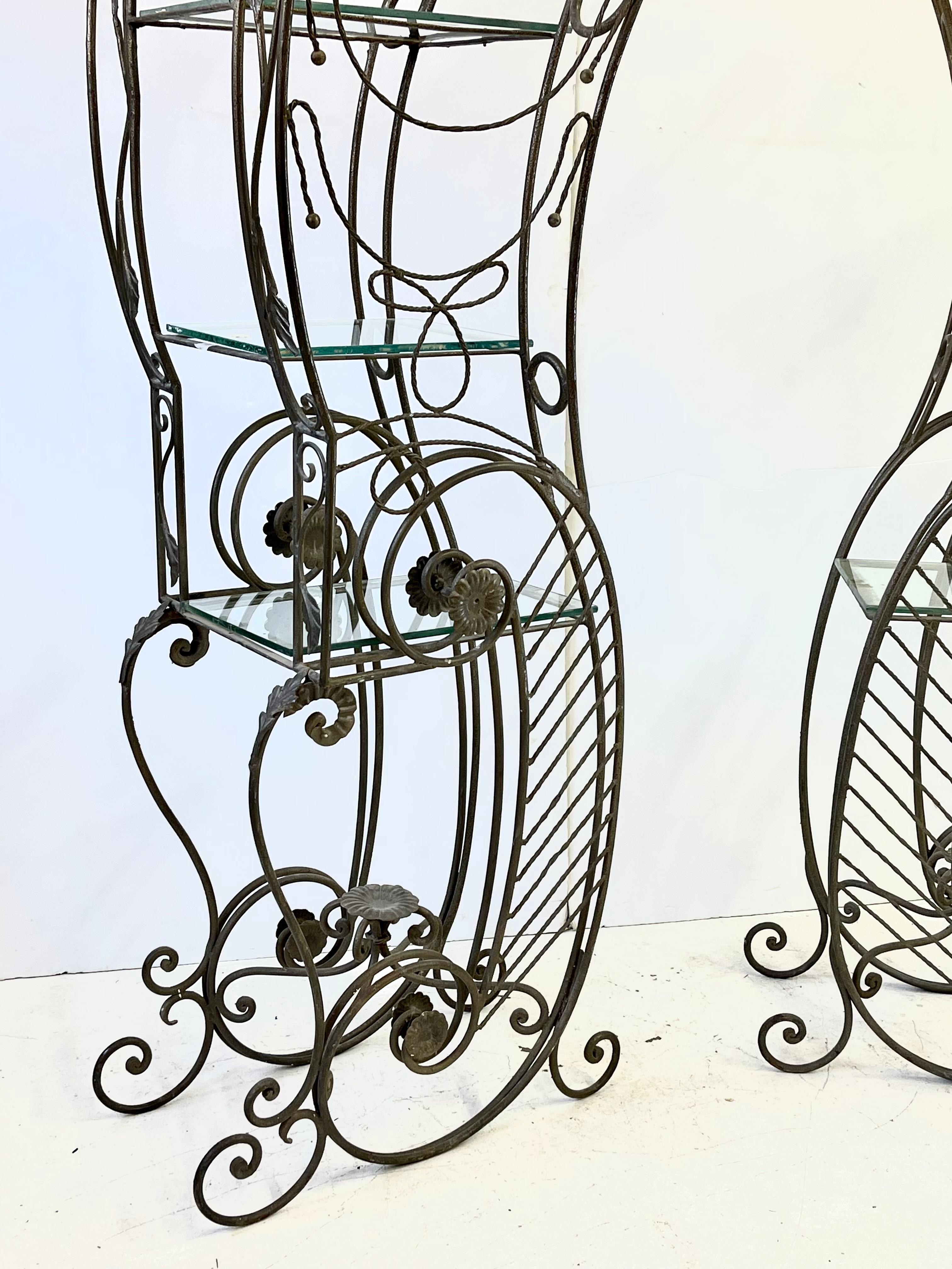 Impressive French early 20th Century facing pair of etageres or baker's racks made of wrought iron in the Art Nouveau style. Each side has three original hand cut glass shelves held by dramatically scrolling iron frames accented by decorative