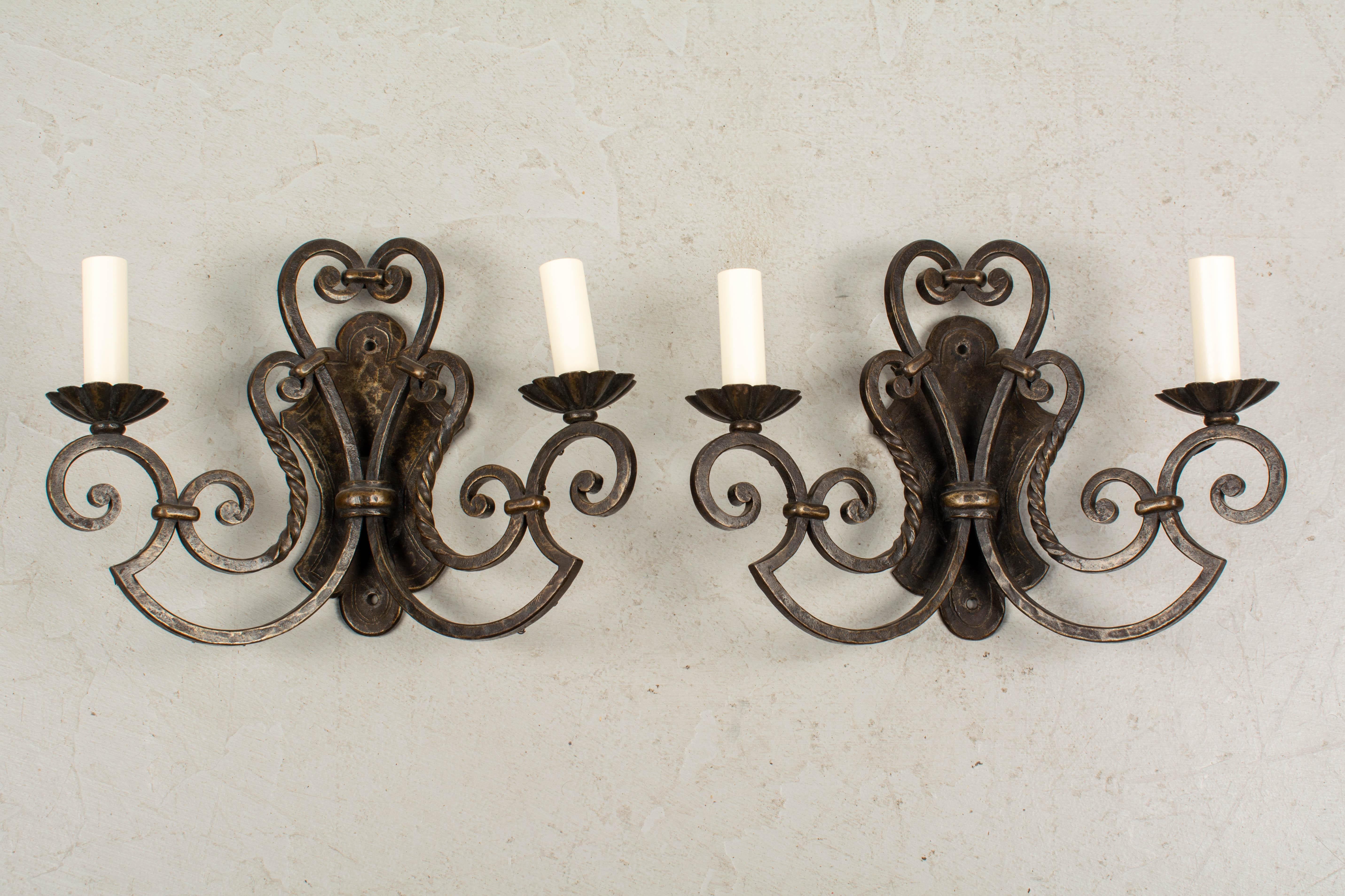 A pair of French wrought iron and two-light sconces with scroll form and bronze patina. Rewired with new sockets and candles covers.