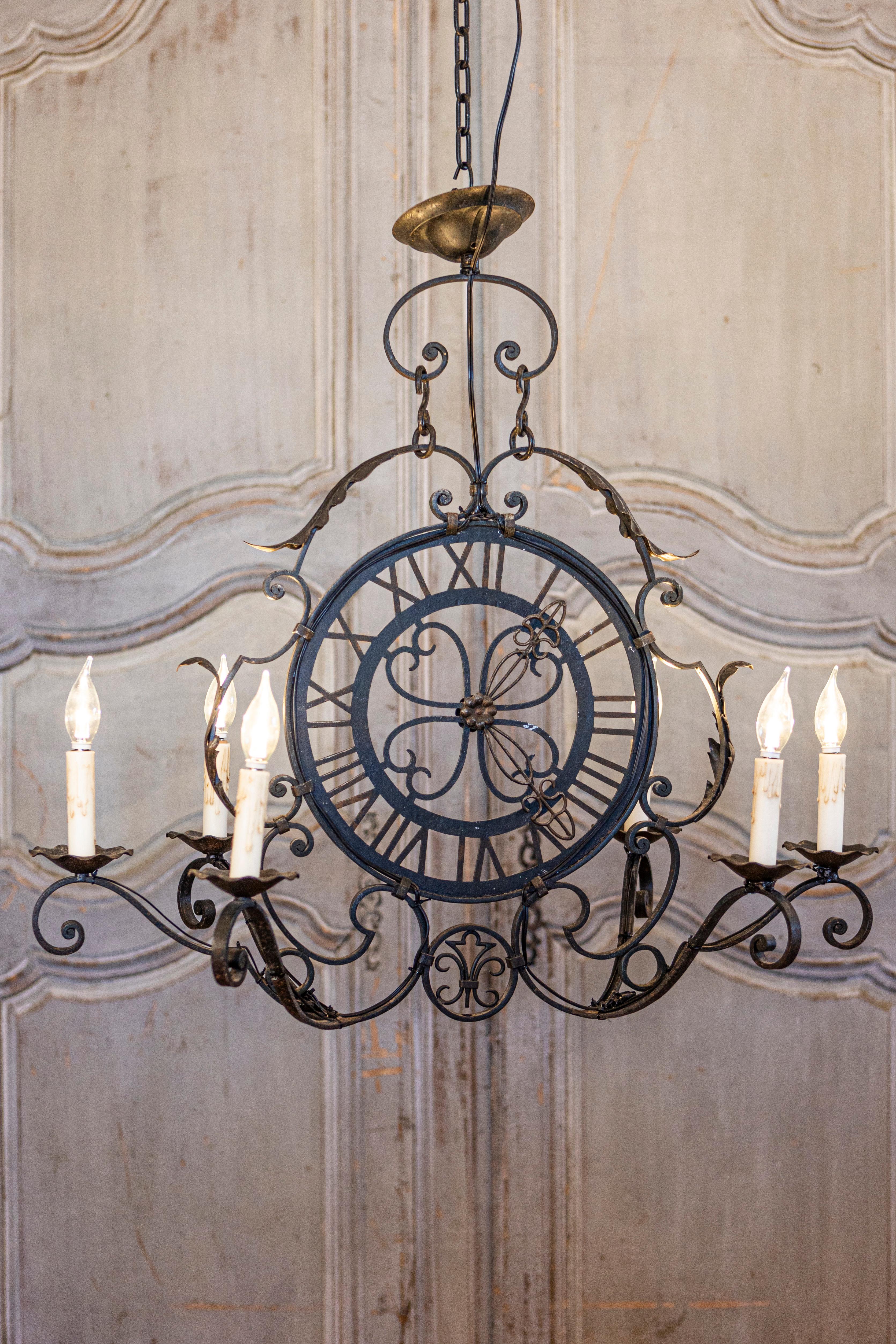 A French wrought-iron clock face chandelier from the 20th century with six scrolling arms and acanthus leaf motifs. This striking French wrought-iron chandelier, originating from the 20th century, marries functionality with artistic design. Its
