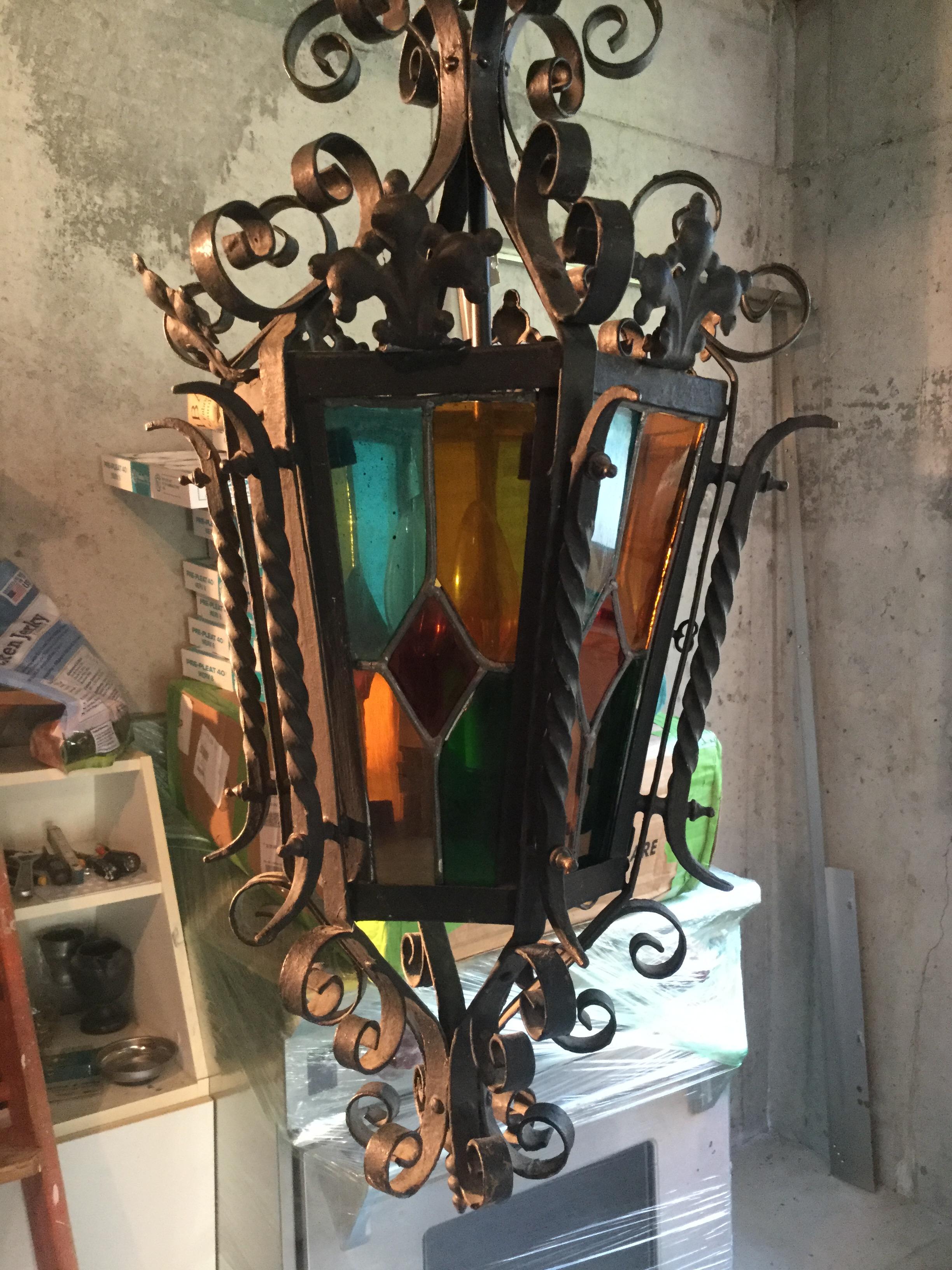 Very old-world iron chandelier features stained-glass that will send vibrant colors of blue, red, and green into your home. Imported from France, this piece is handcrafted from iron and real stained-glass. One of the glass panels opens in order to