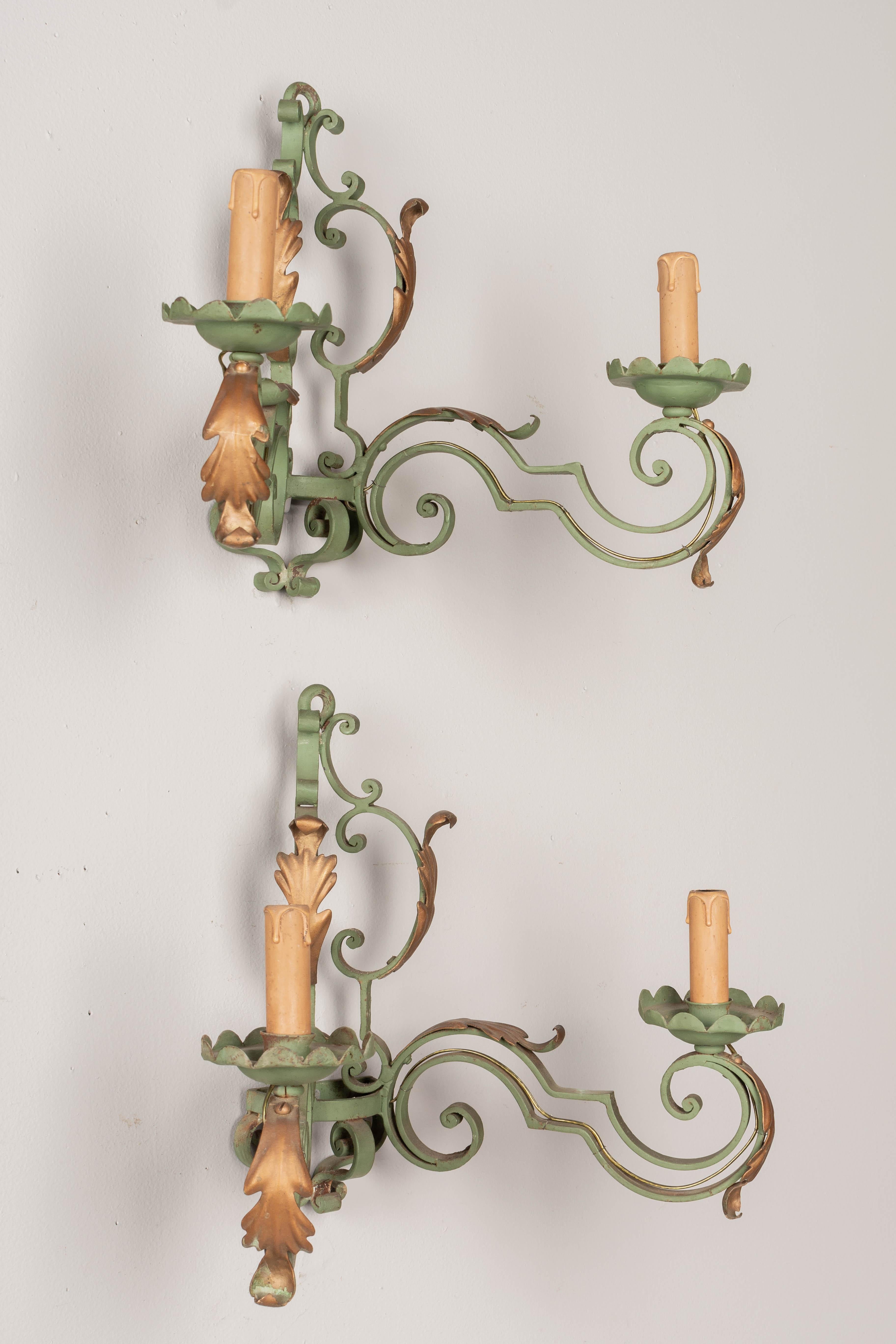 A pair of French wrought iron two-light sconces with verdigris painted patina. Scroll form with gilt tole acanthus leaves. Original candle covers. Rewired with new sockets. 
