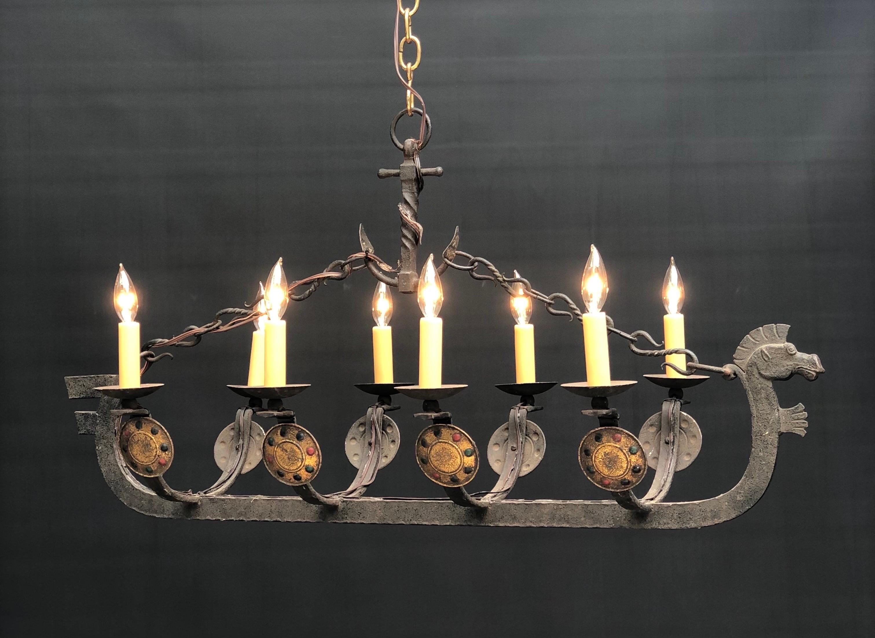 French wrought iron Viking dragon ship chandelier has eight candelabra arms with gilt Viking Shields on each arm. This wonderful ship chandelier is suspended by two hand wrought S chains coming from a hand wrought ships anchor. These dragon