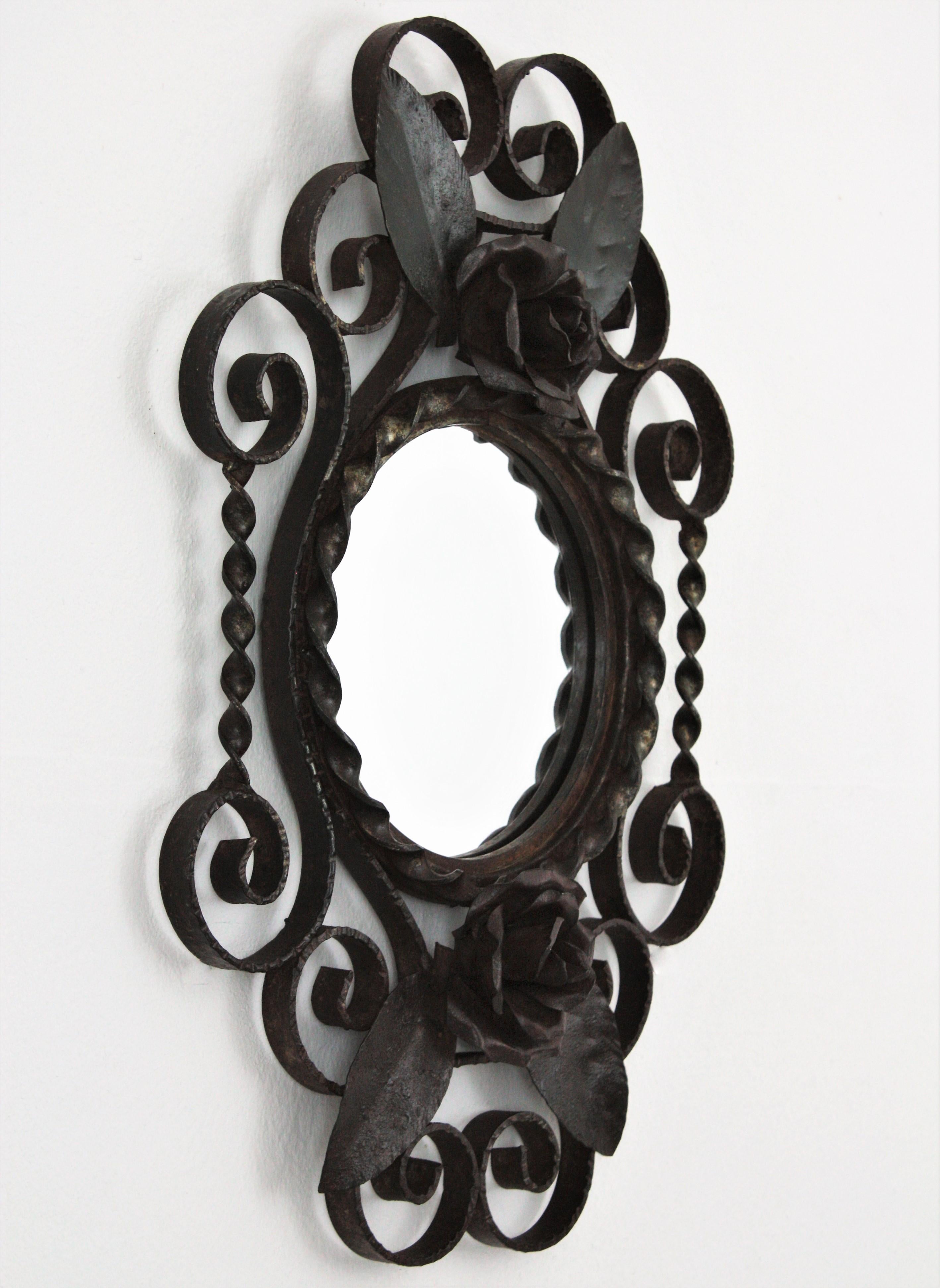 Lovely petite hand forged wall mirror with floral and scroll details. France, 1940s.
This iron mirror is all made by hand. It has scroll and twisted iron decorations surrounding a central round glass and two iron roses with leaves accenting the top