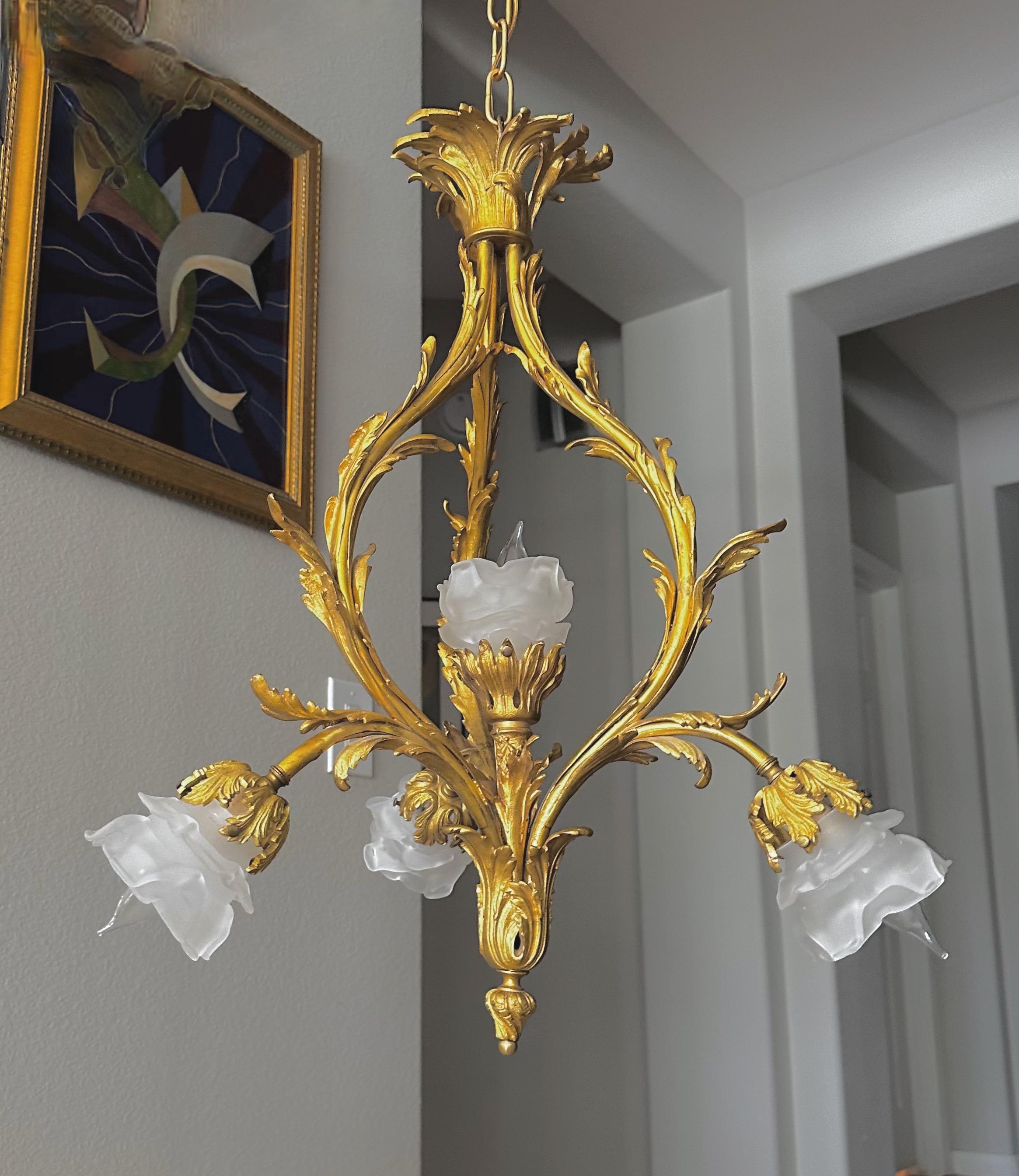 Pendelleuchte oder Kronleuchter aus vergoldeter Bronze im Stil Louis XV mit Rokoko-Einfluss. Rosenknospenschirme aus mattiertem Glas auf 5 verschnörkelten Armen mit blattförmigen Details. Für 5 Glühbirnen in Kandelabergröße, neu verdrahtet. 
Größe