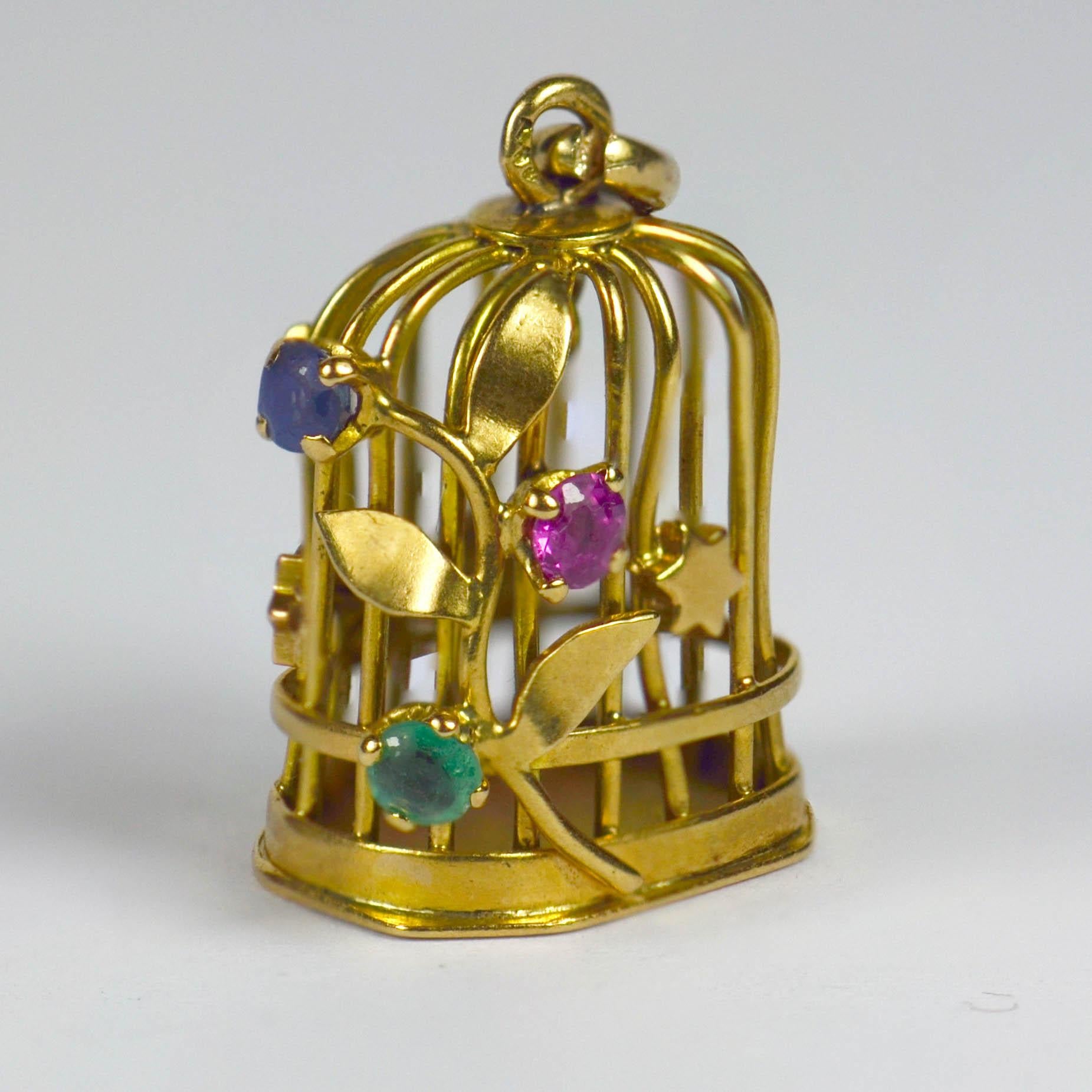 A French 18 karat yellow gold charm pendant designed as a bird cage with gem set flowering vine and stars, and a gold bird on a perch inside. Set with blue green and pink round cut paste, the charm is stamped with the eagle's head for 18 karat gold