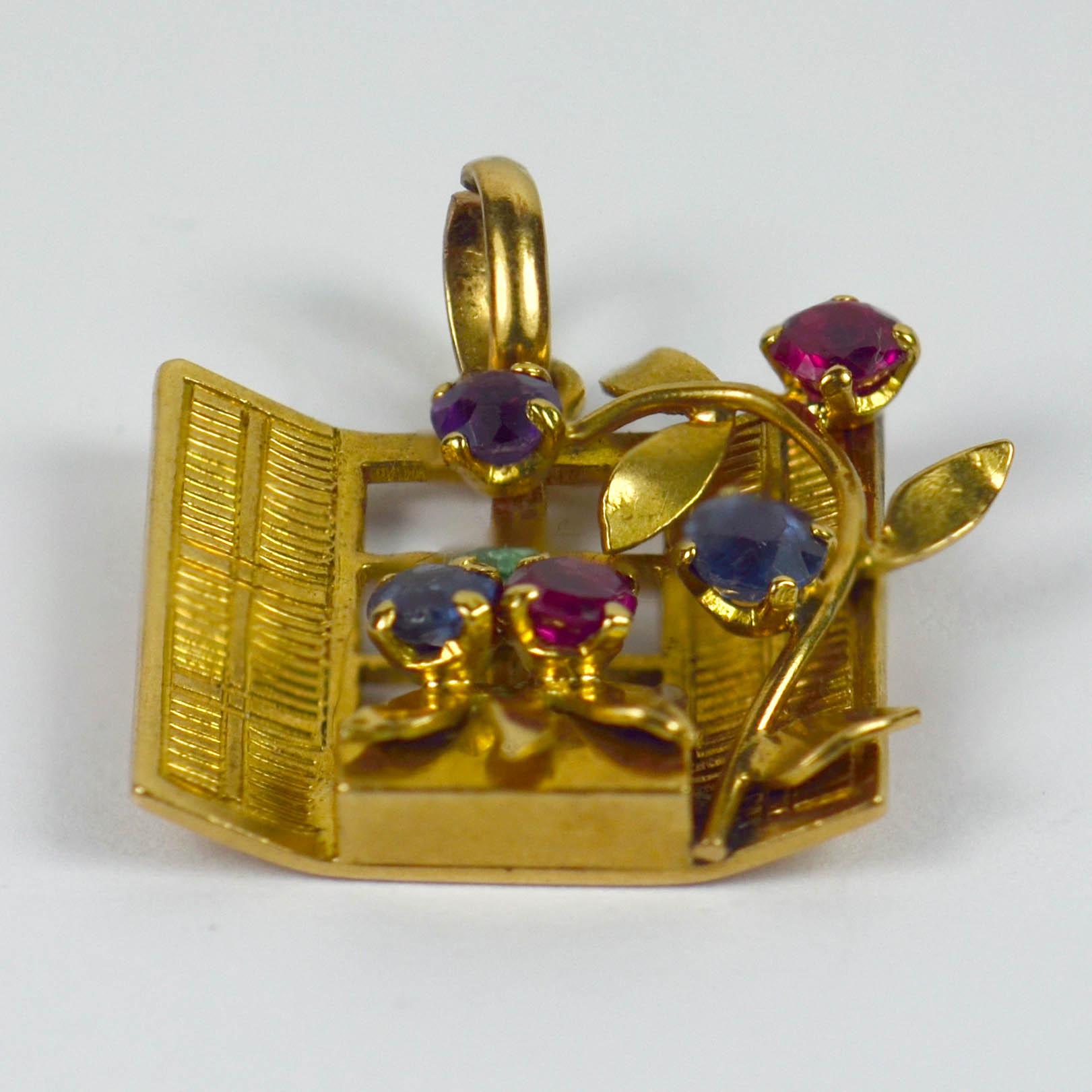 A French 18 karat yellow gold charm pendant designed as an open window with gem set flowering vine and flower box. Stamped with the eagles head for French manufacture and 18 karat gold, and set with red, purple, green and blue round cut