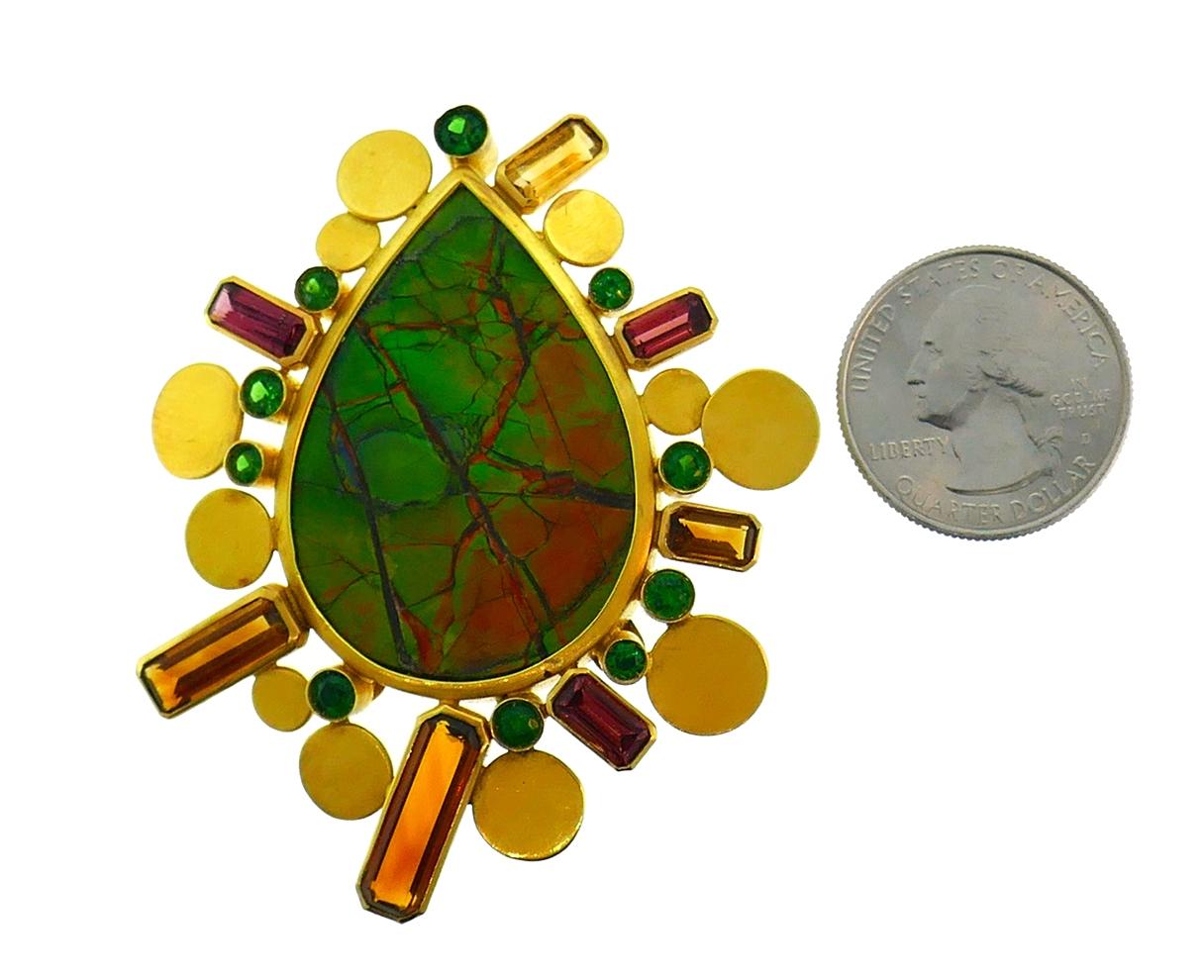 Colorful and bold clip/pendant created by Christine Escher in France in the 1990s. 
Made of 18 karat yellow gold, the brooch features a pear-shape ammolite accented with faceted garnet.
Measurements: 2-1/2 x 2-1/8 inches (6.5 x 5.4 cm).
Weight: 40.0