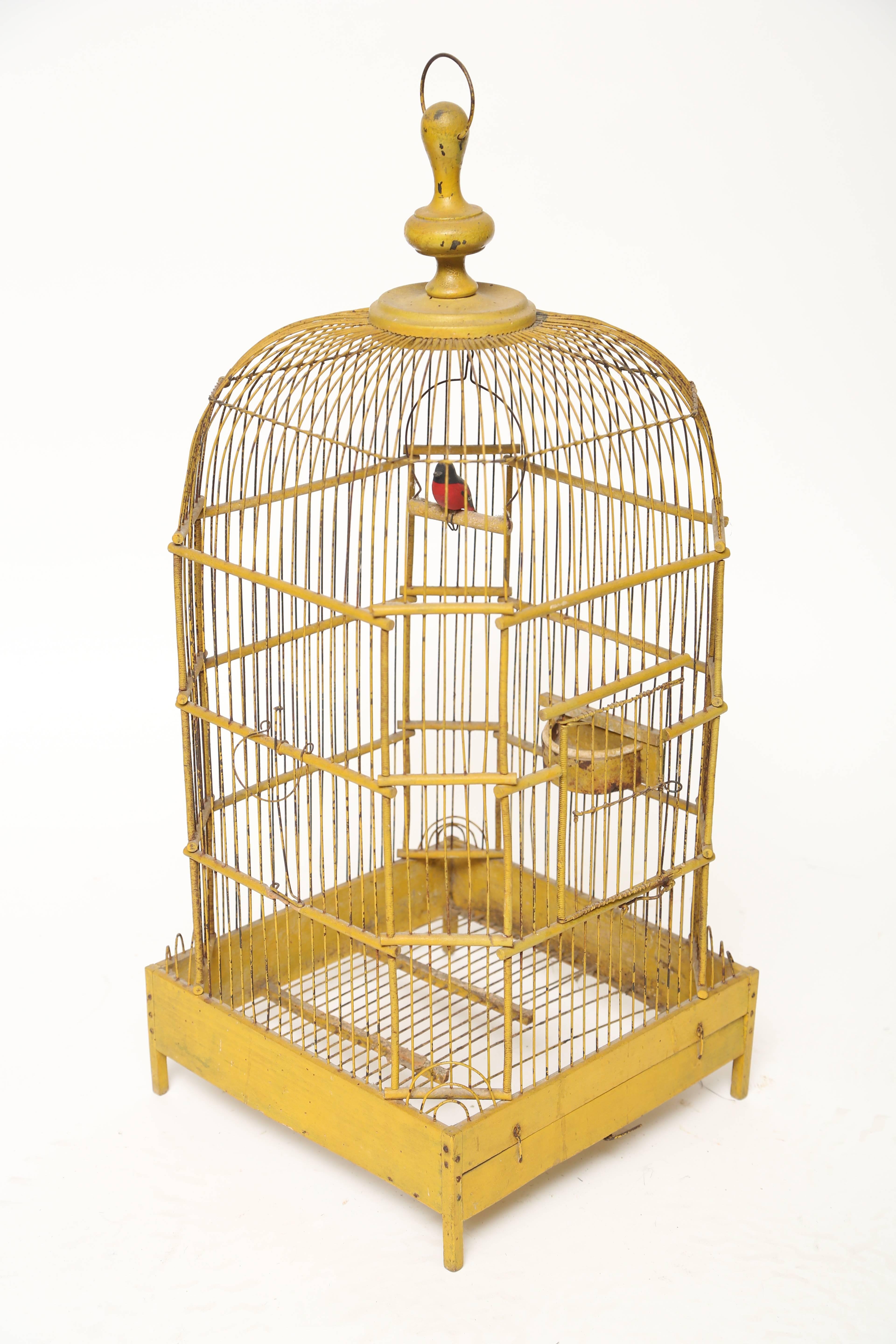 Dome toped French ochre bird cage on four legs, original feeder and door centre front. There is a large turned finial at the top and a faux bird within on its perch.  If you want that south of France feeling this piece has it.