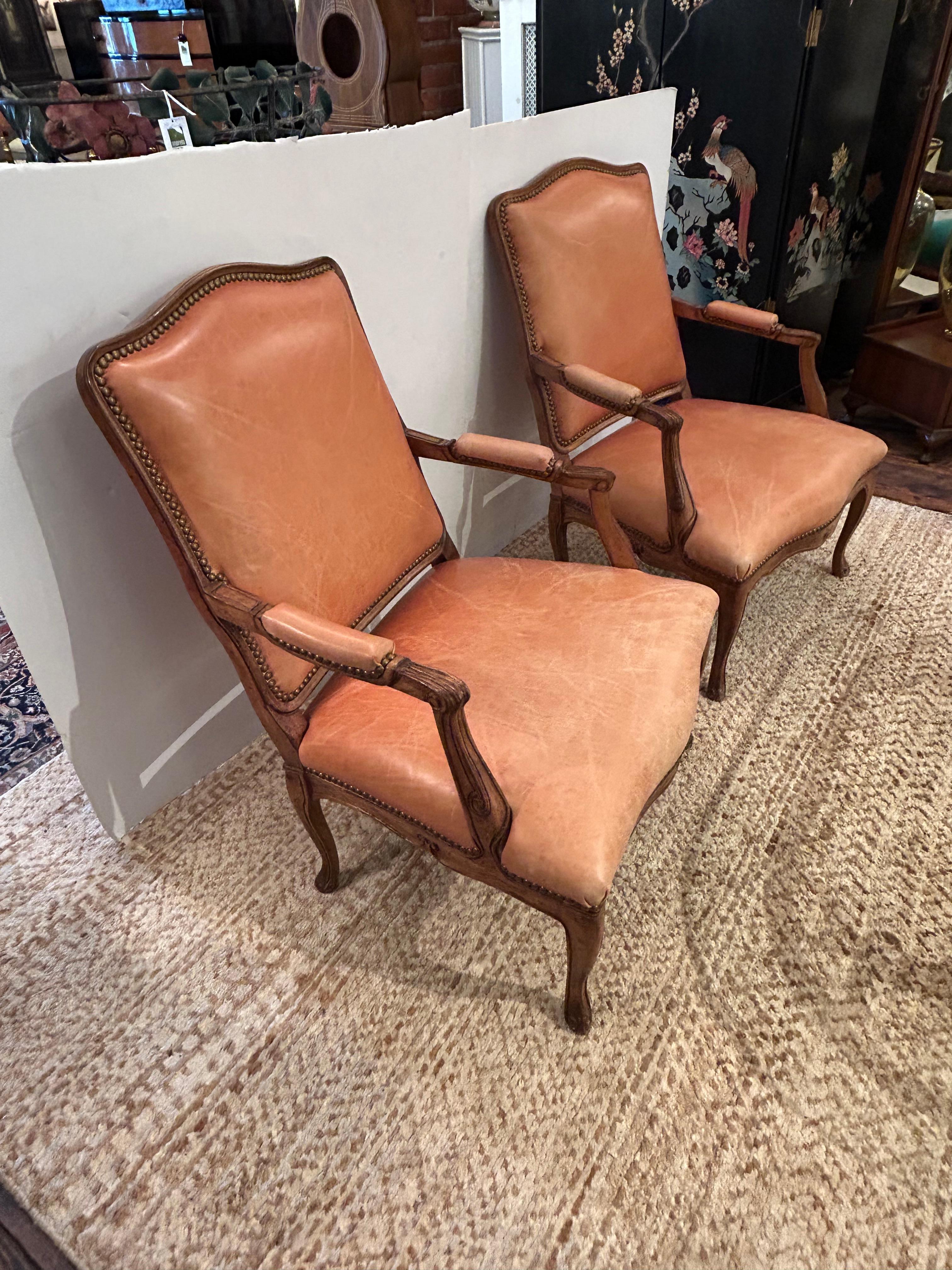 Bellissima coppia di grandi e comode poltrone in noce intagliato con un morbido rivestimento in pelle marrone chiaro arancione e rifinite con teste di chiodi in ottone anticato.  Gli schienali sono rivestiti in un tessuto di seta a righe.
Altezza