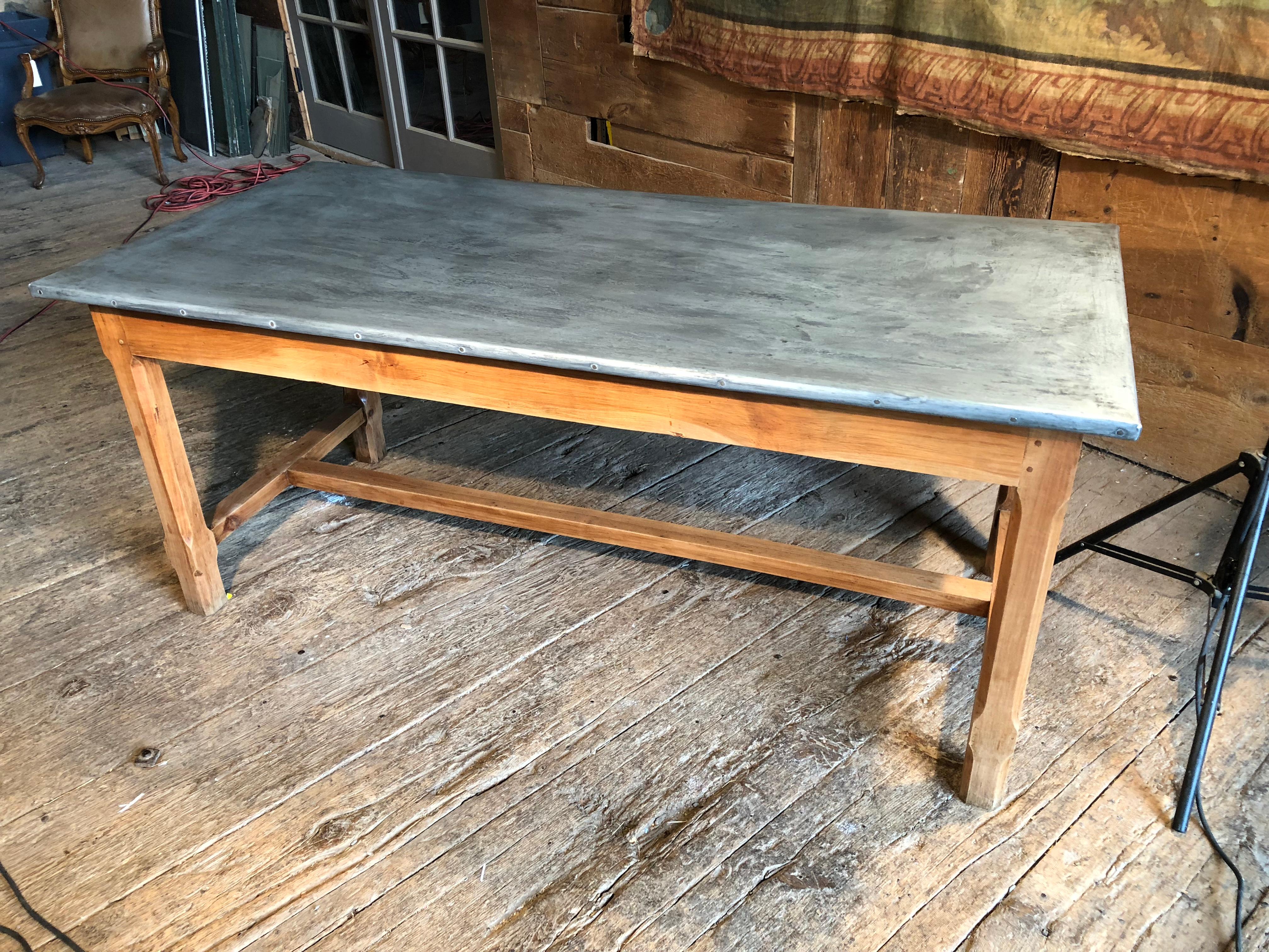 A mid-19th century French zinc top trestle table in fruitwood with a drawer on one end and a cutting board on the other, the chamfered legs supported with stretchers.