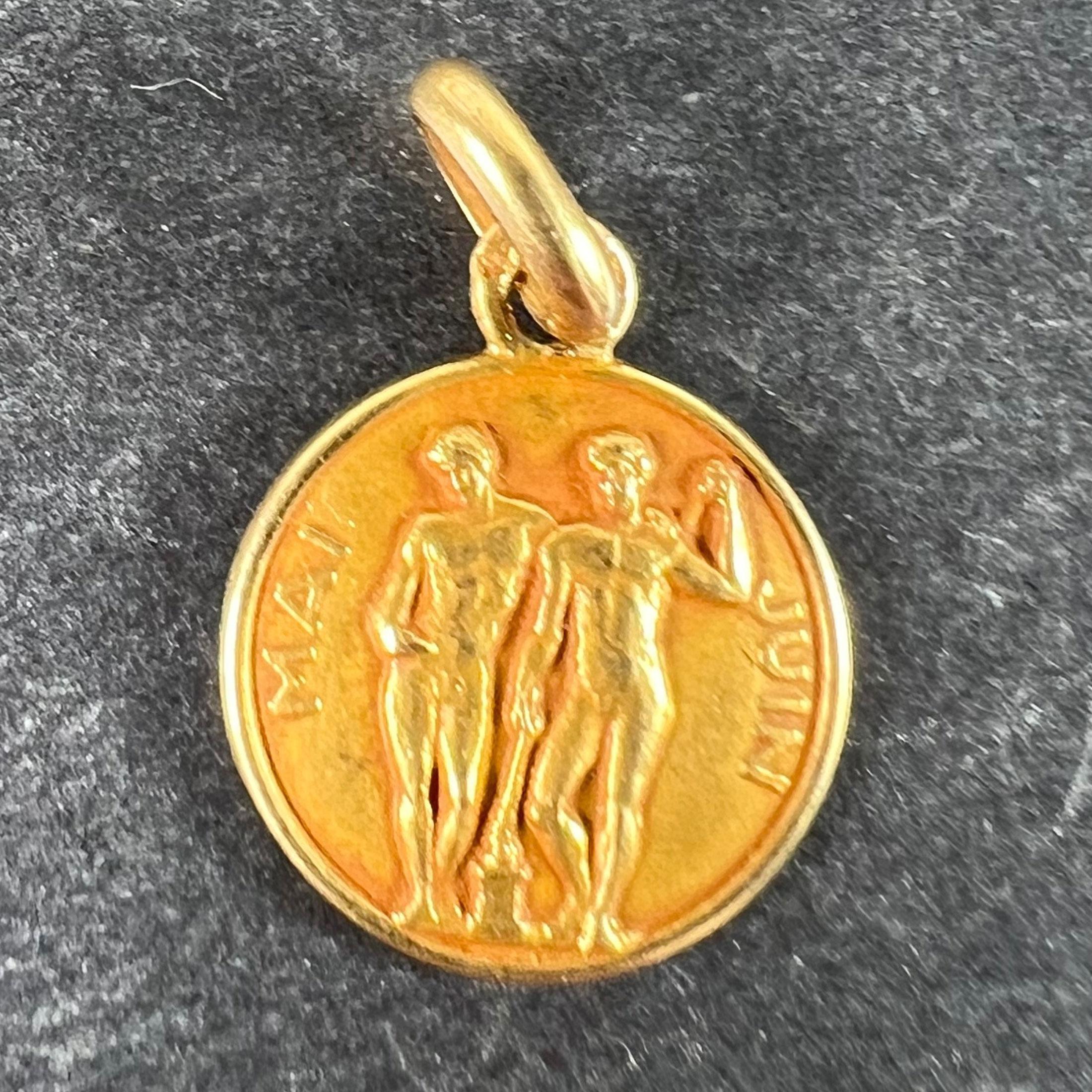 A small French 18 karat (18K) yellow gold charm pendant designed as a medal depicting the Zodiac sign of Gemini, showing a pair of twins modelled in the style of Greek statues, with the words 'Mai' and 'Juin' to each side. Stamped with the French