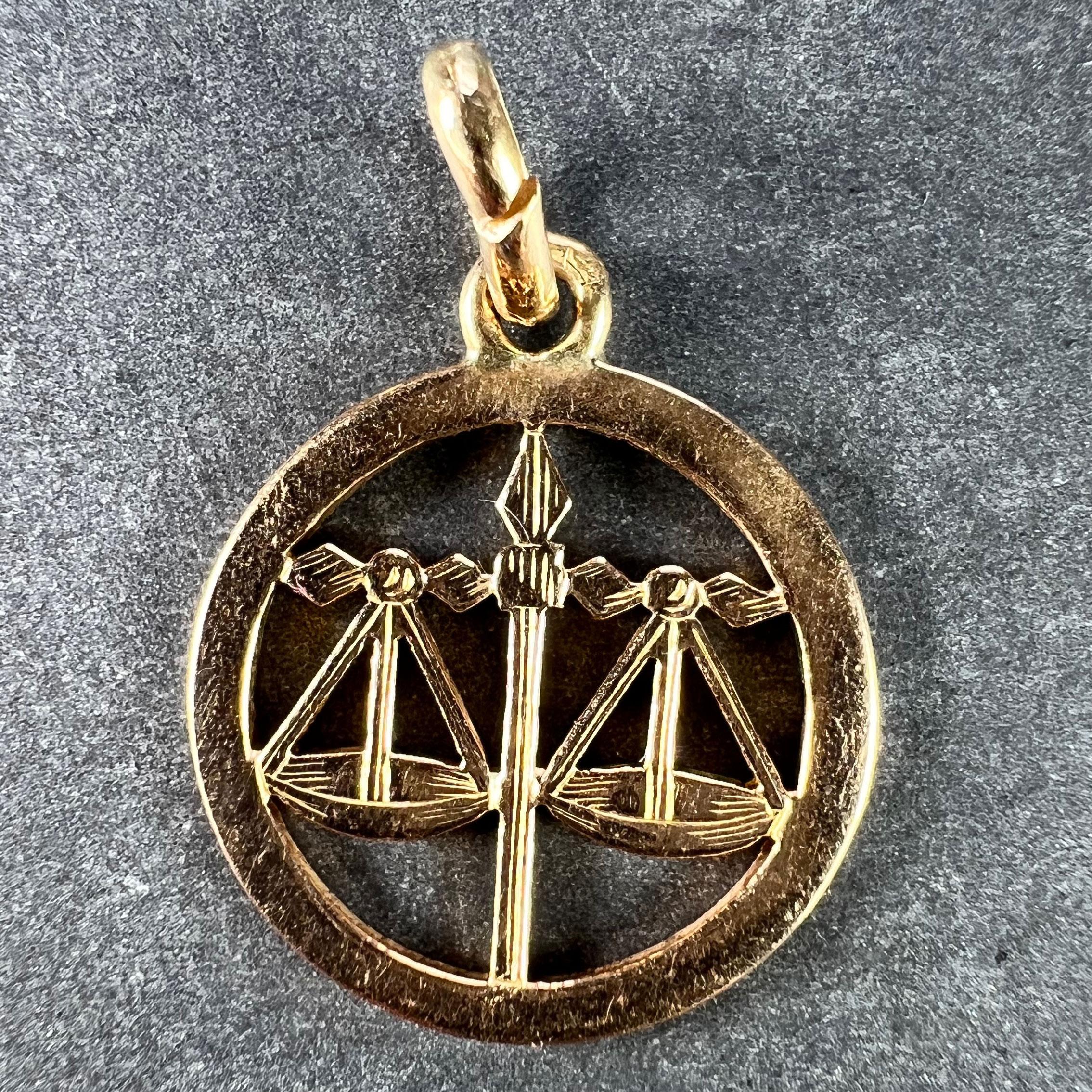A French 18 karat (18K) yellow gold charm pendant designed as a circular disc with cut-out areas depicting a set of balance scales representing the zodiac star sign of Libra. Stamped with the eagle’s head for French manufacture and 18 karat
