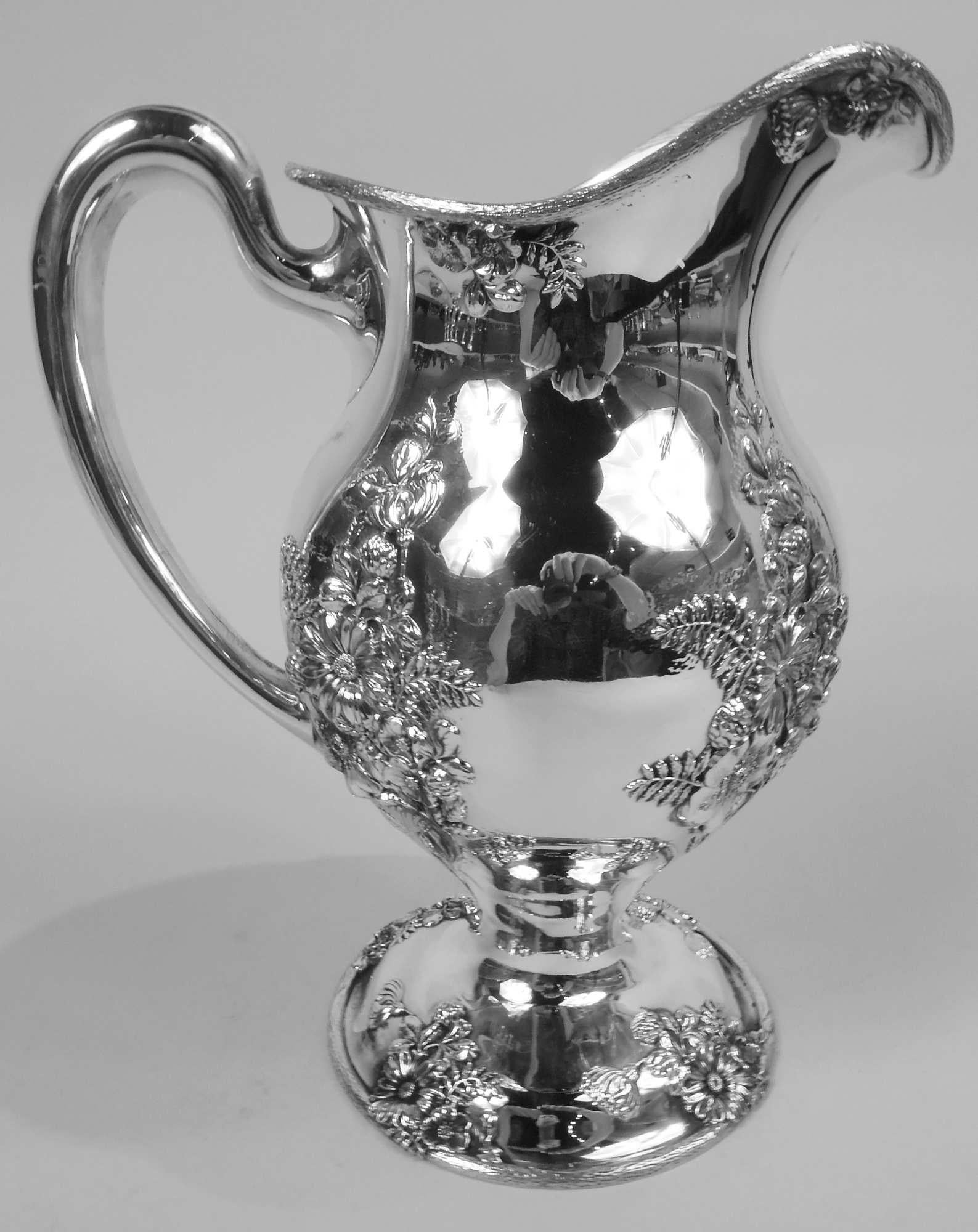 Fresh and Pretty American Art Nouveau sterling silver water pitcher, ca 1910. Retailed by Udall & Ballou in New York. Lobed and ovoid body with helmet mouth, domed foot, and high-looping handle. Applied and chased flower and frond clusters on body